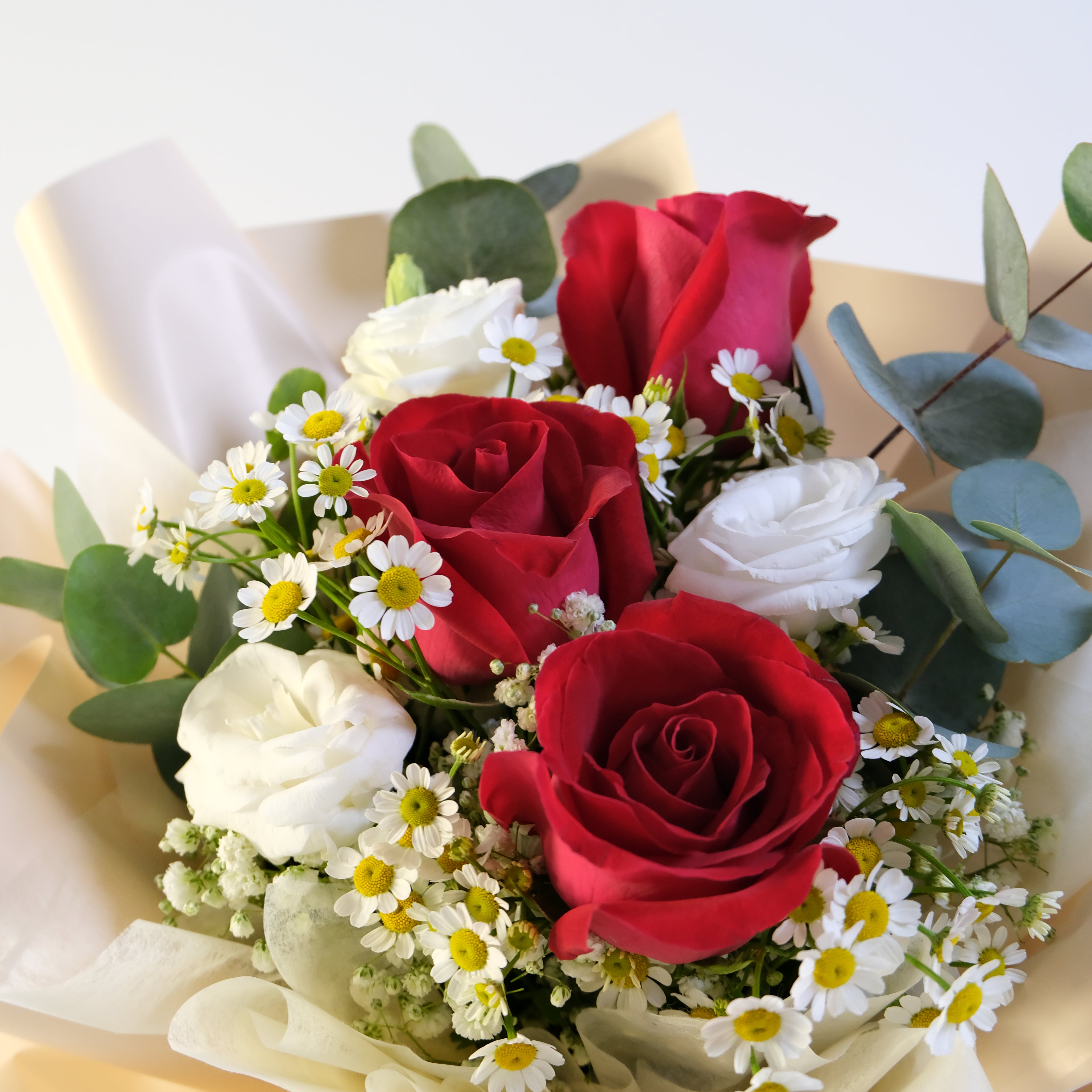 Bouquet of red roses, white flowers, and greenery on a light background