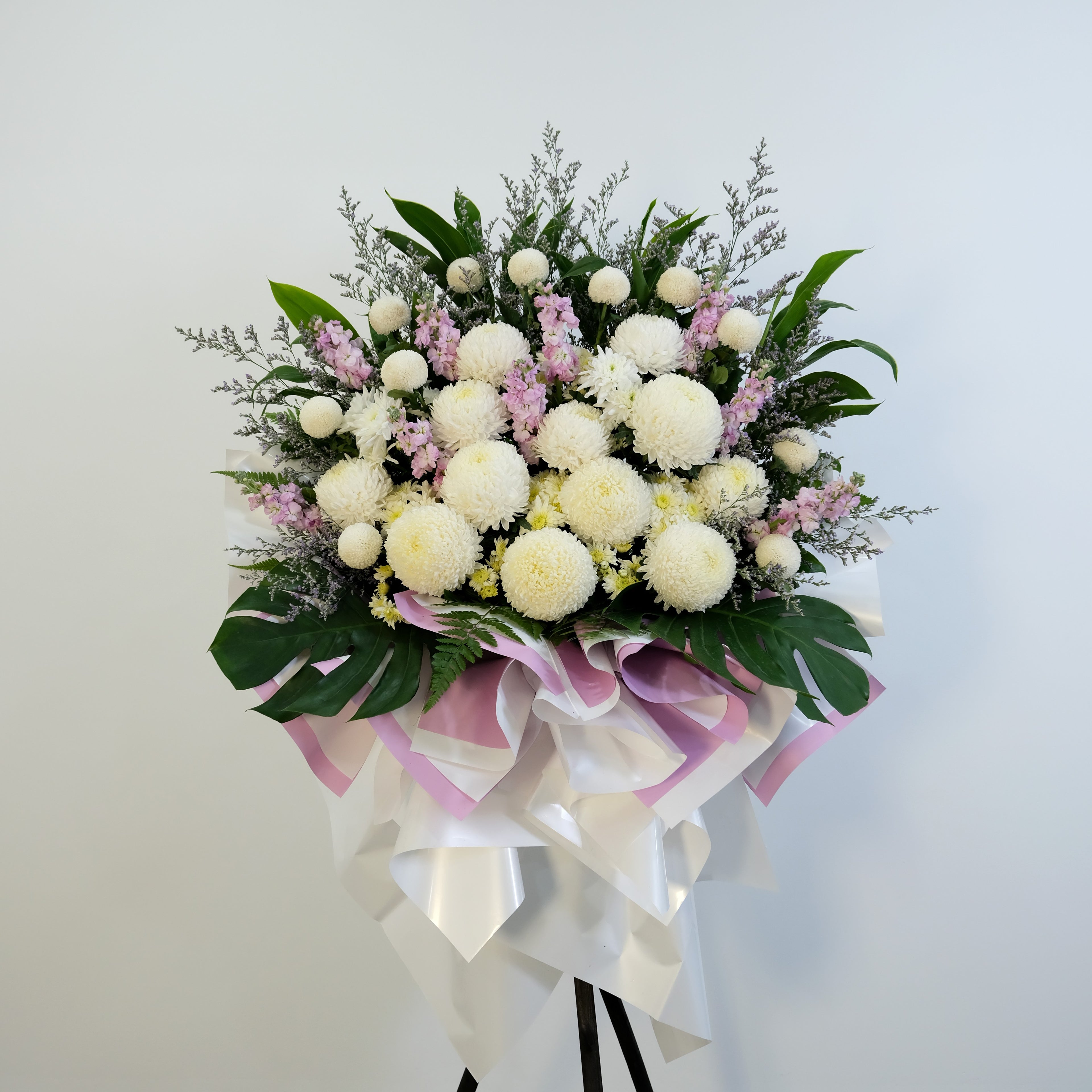 condolence flowe stand of white and pink flowers with greenery on a stand against a light gray background