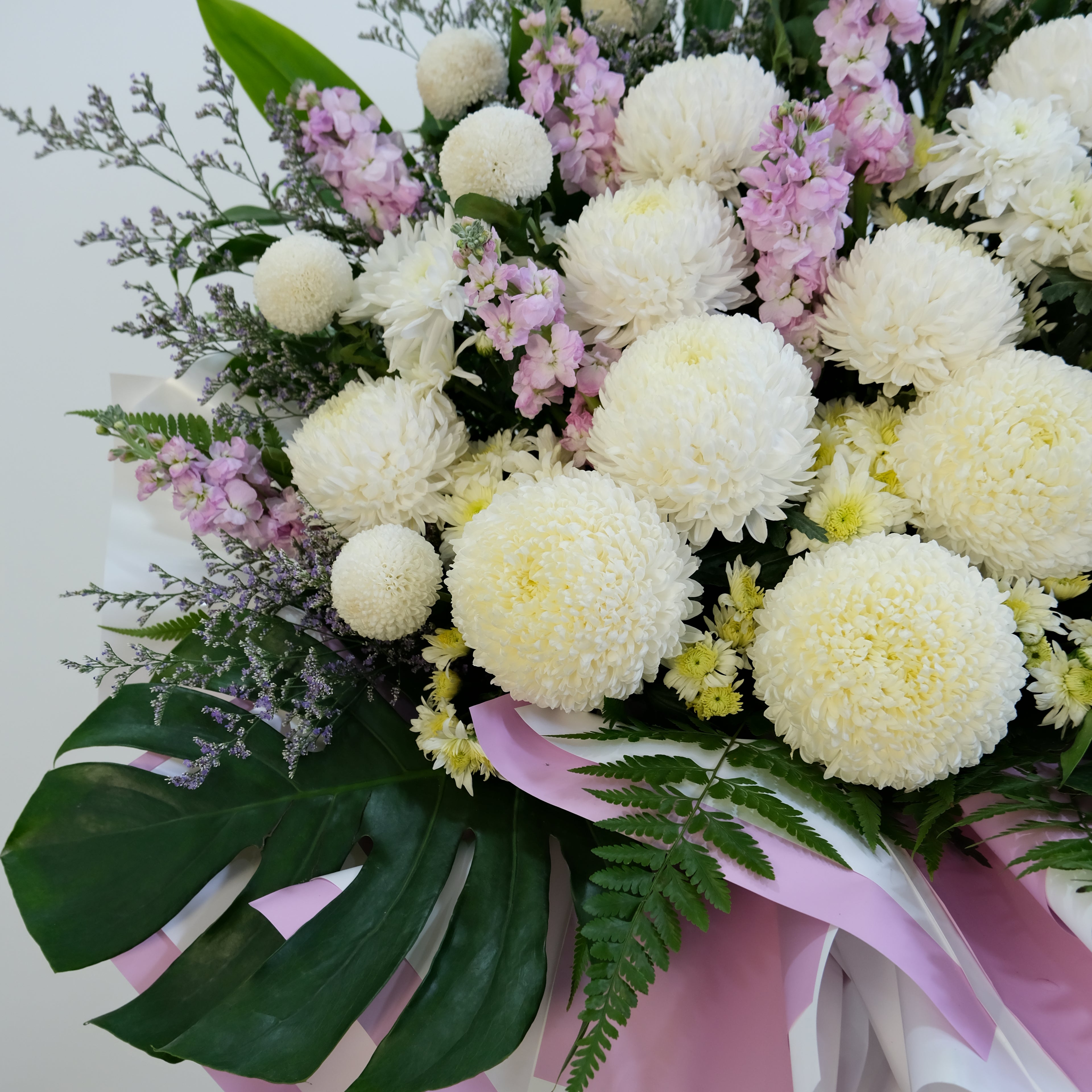 Bouquet of flowers with white and pink flowers, green leaves, and a pink ribbon on a white background.