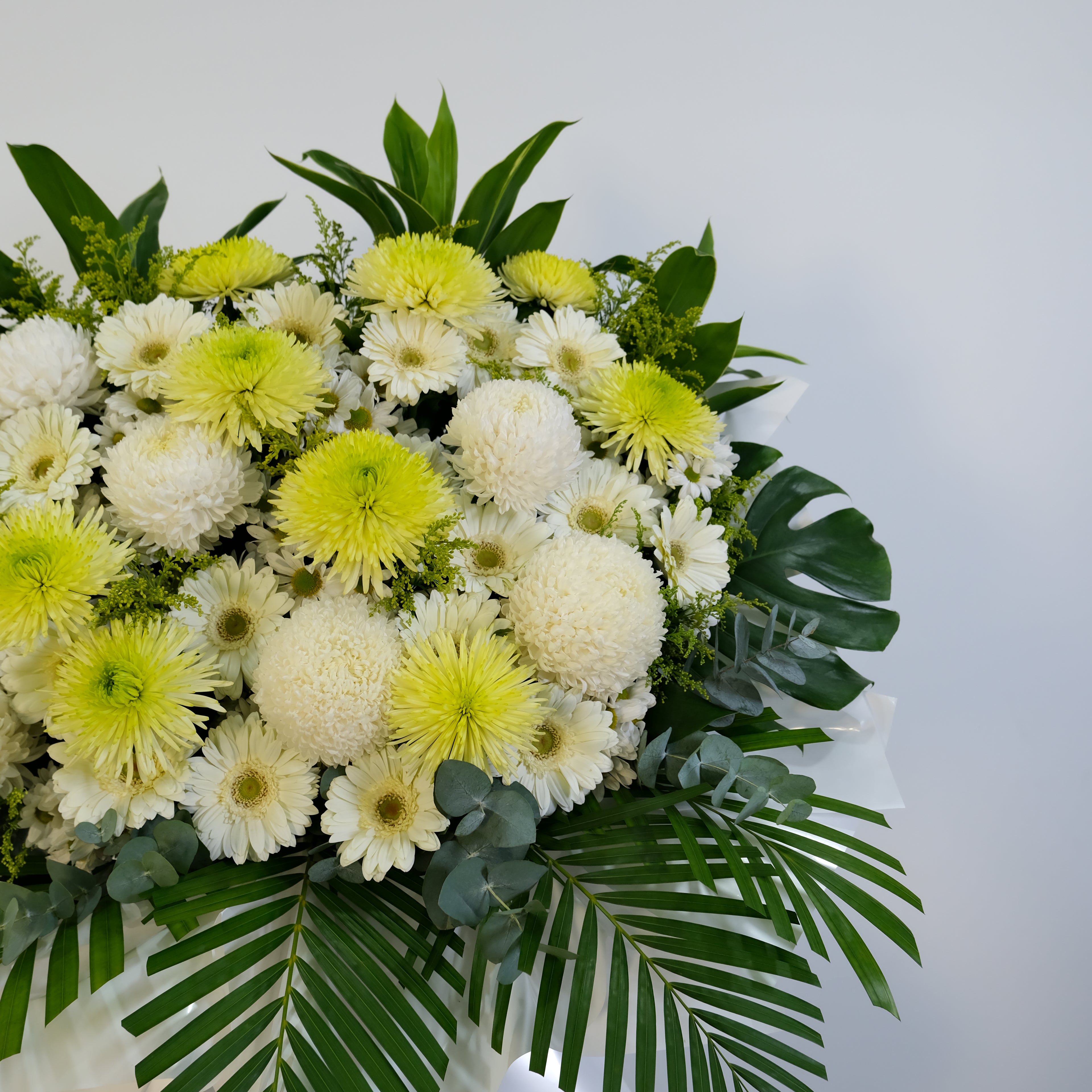 Floral arrangement with white and yellow flowers and green leaves on a light gray background