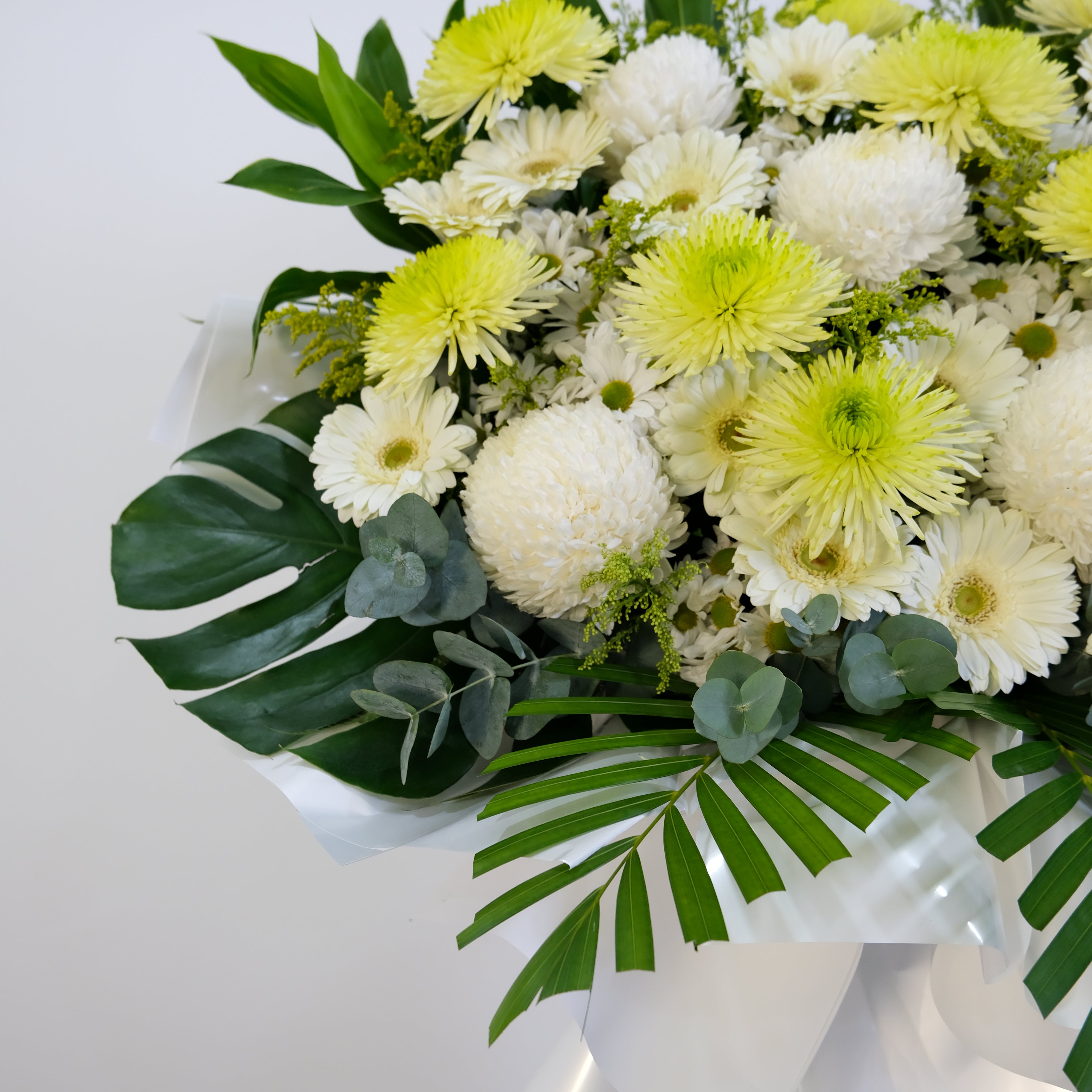 Bouquet of white and yellow flowers with green leaves in a white box.
