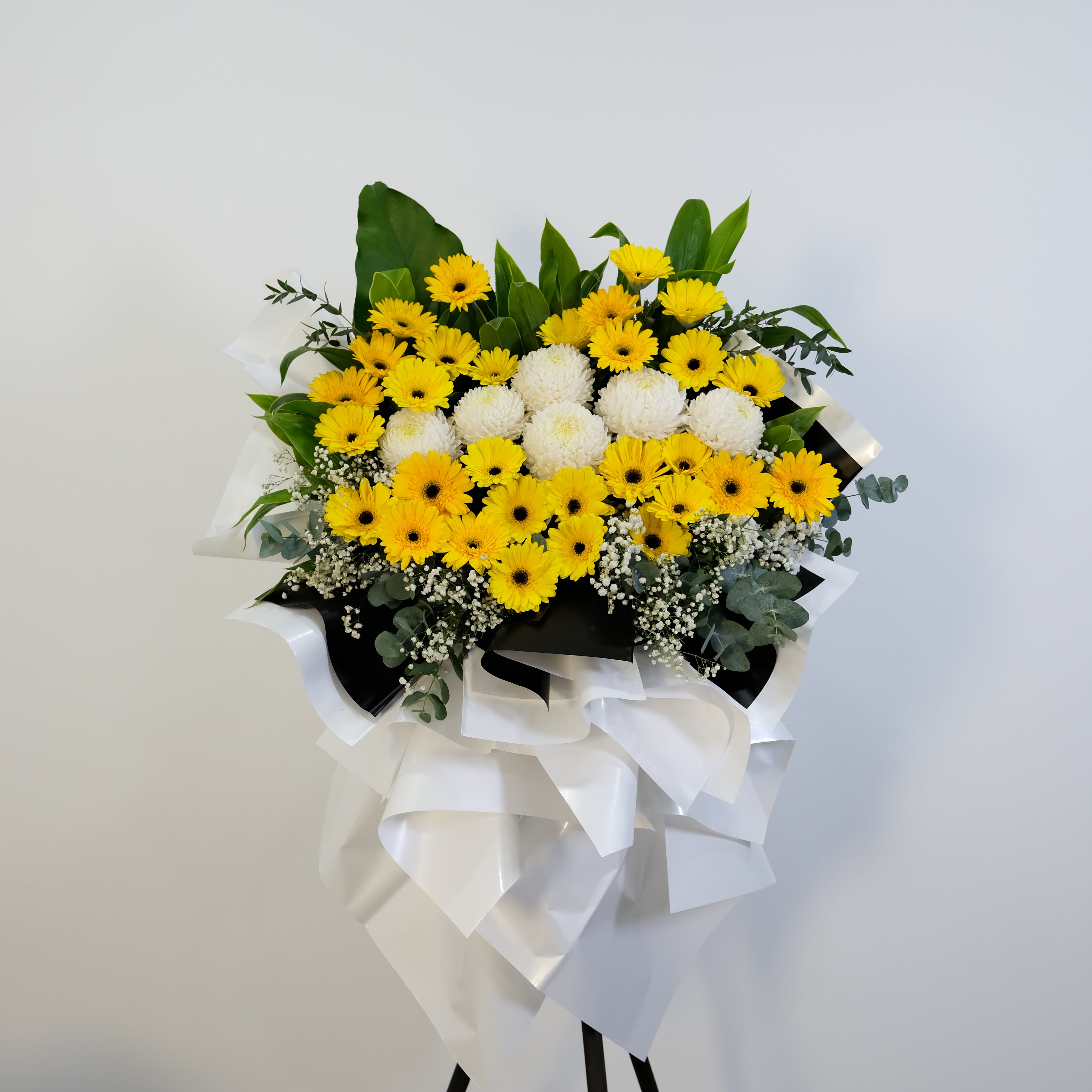 Bouquet of yellow and white flowers with a large white bow on a light gray background