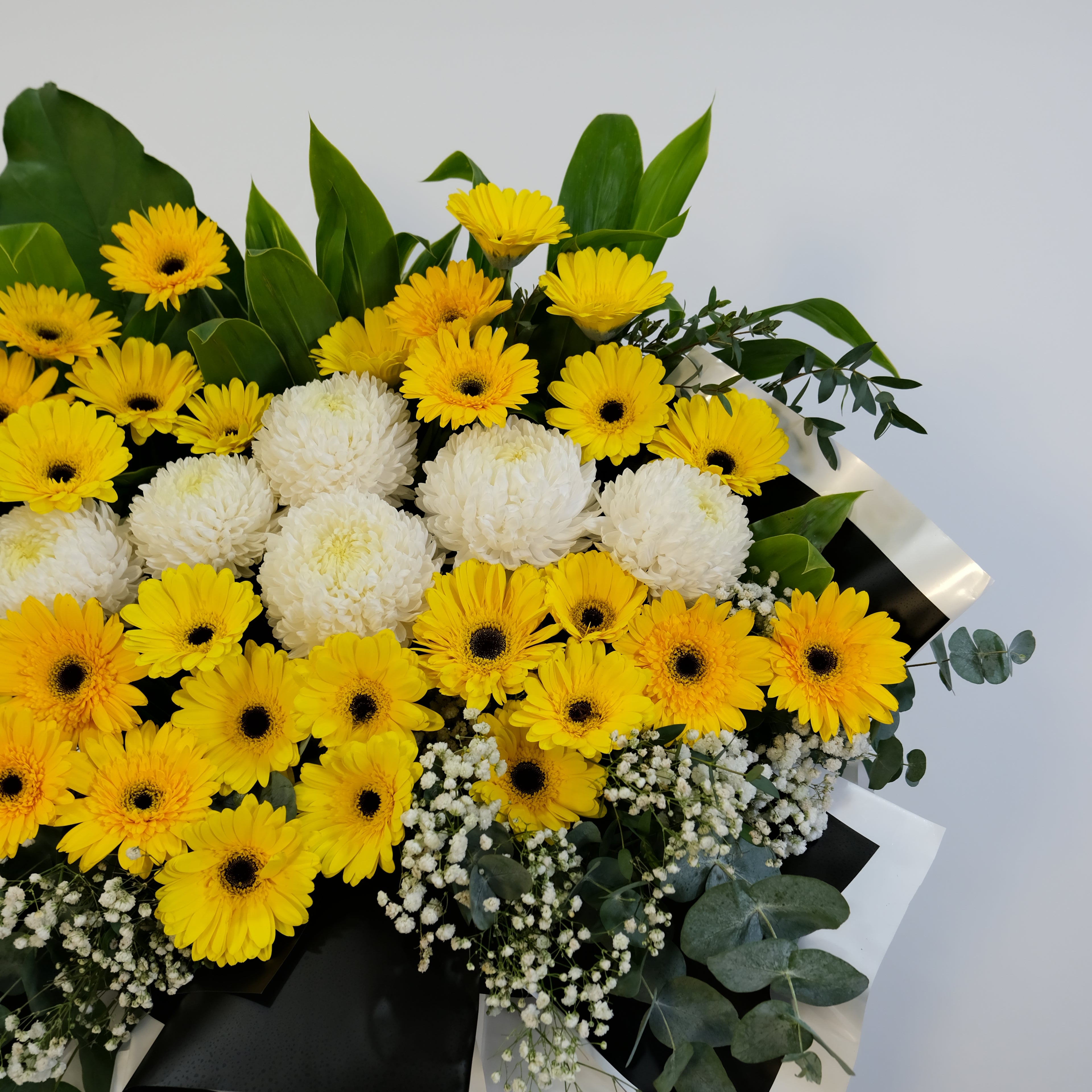 condolence flower stand Bouquet of yellow and white flowers with green leaves on a light gray background