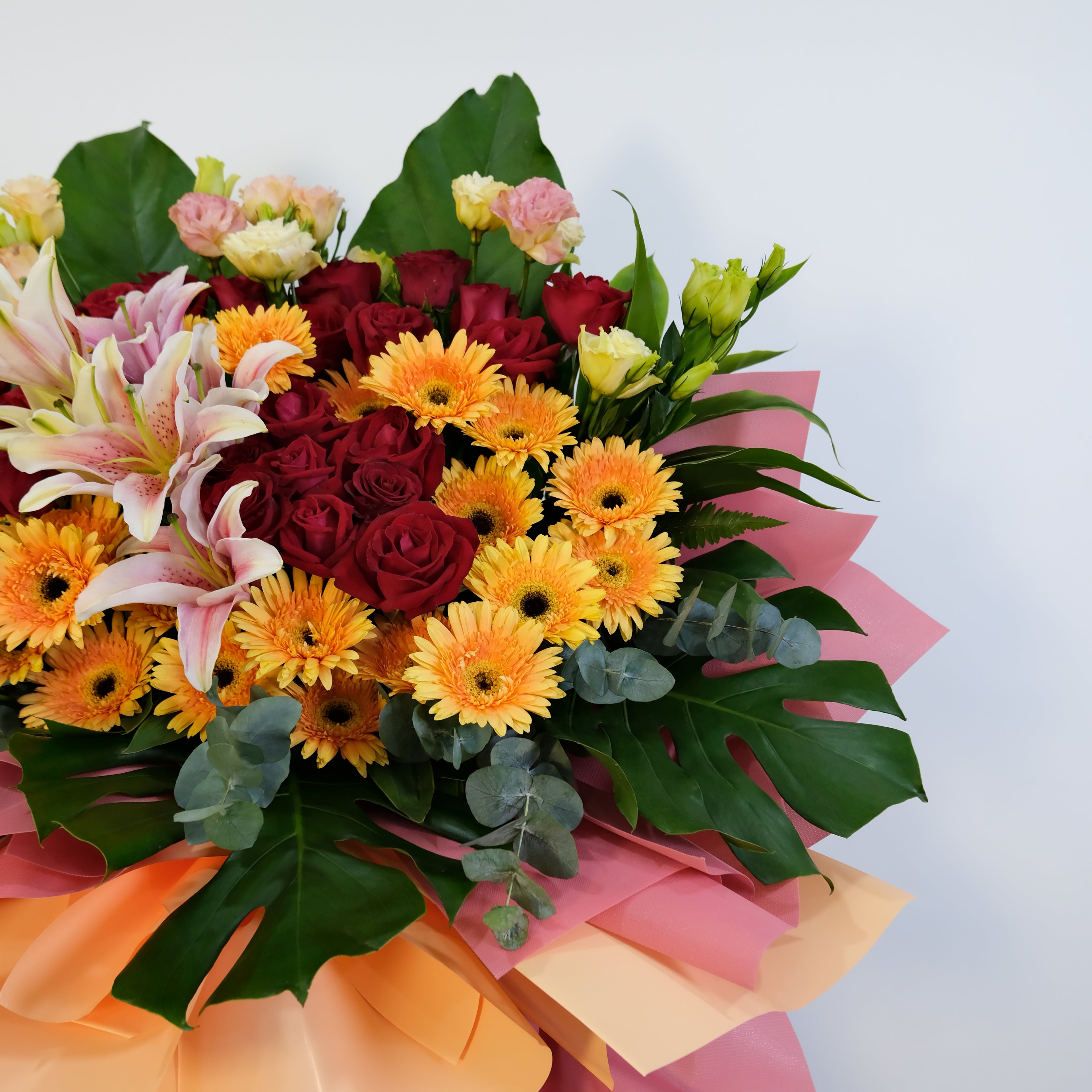 Bouquet of flowers with red roses, yellow daisies, and pink lilies on a light gray background.
