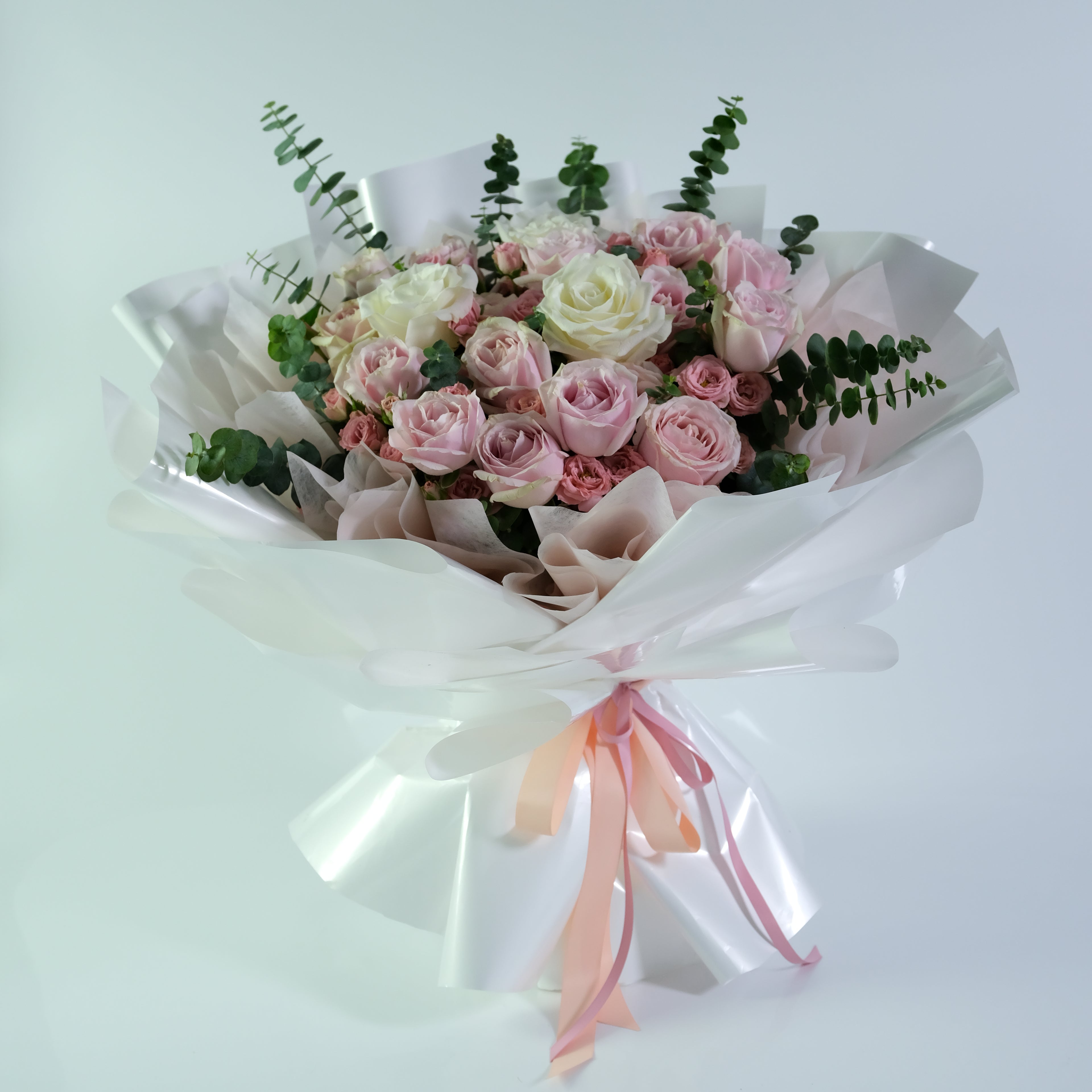 Bouquet of pink and white roses with greenery on a light gray background