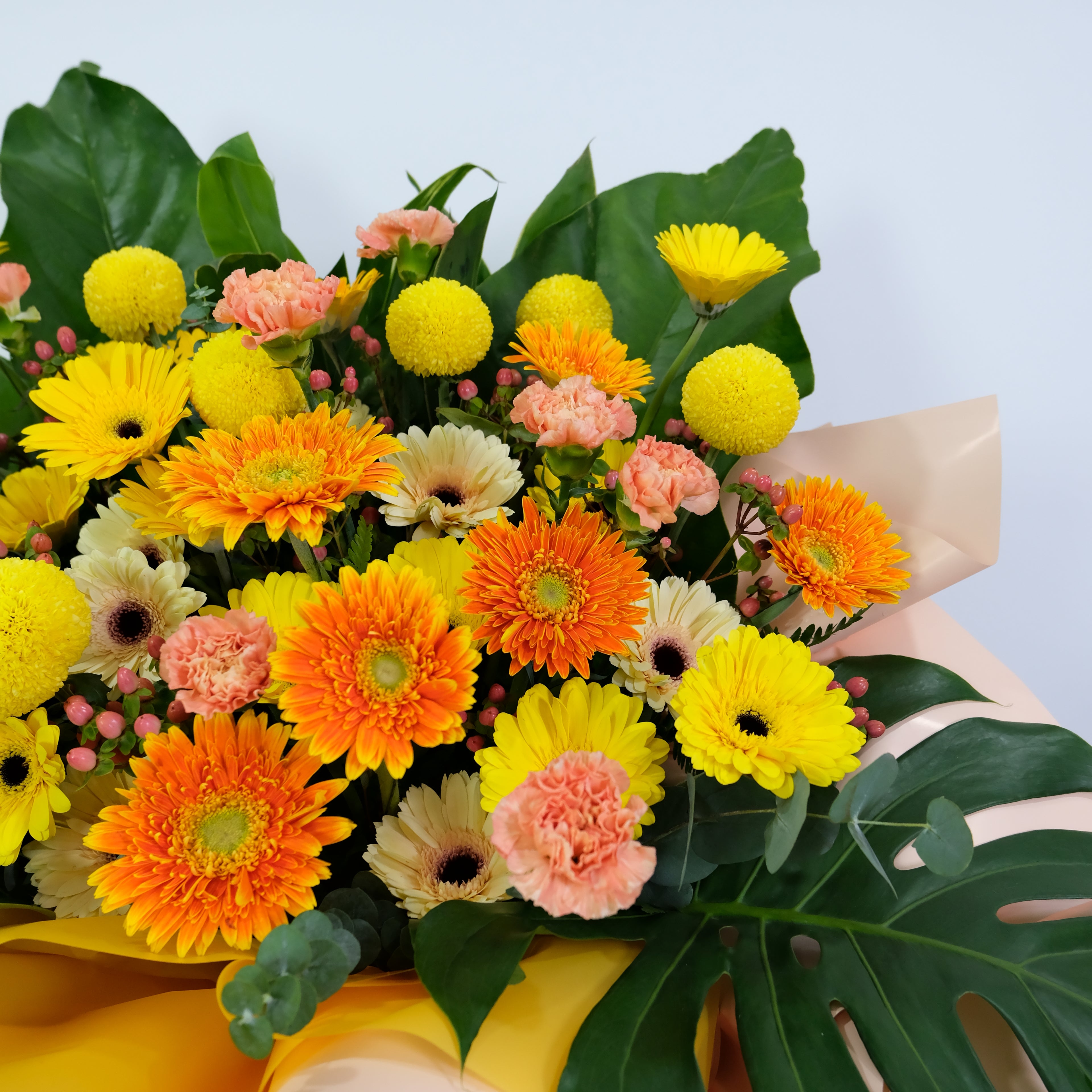 Bouquet of colorful flowers including oranges, yellows, and pinks held by a hand against a light blue background.