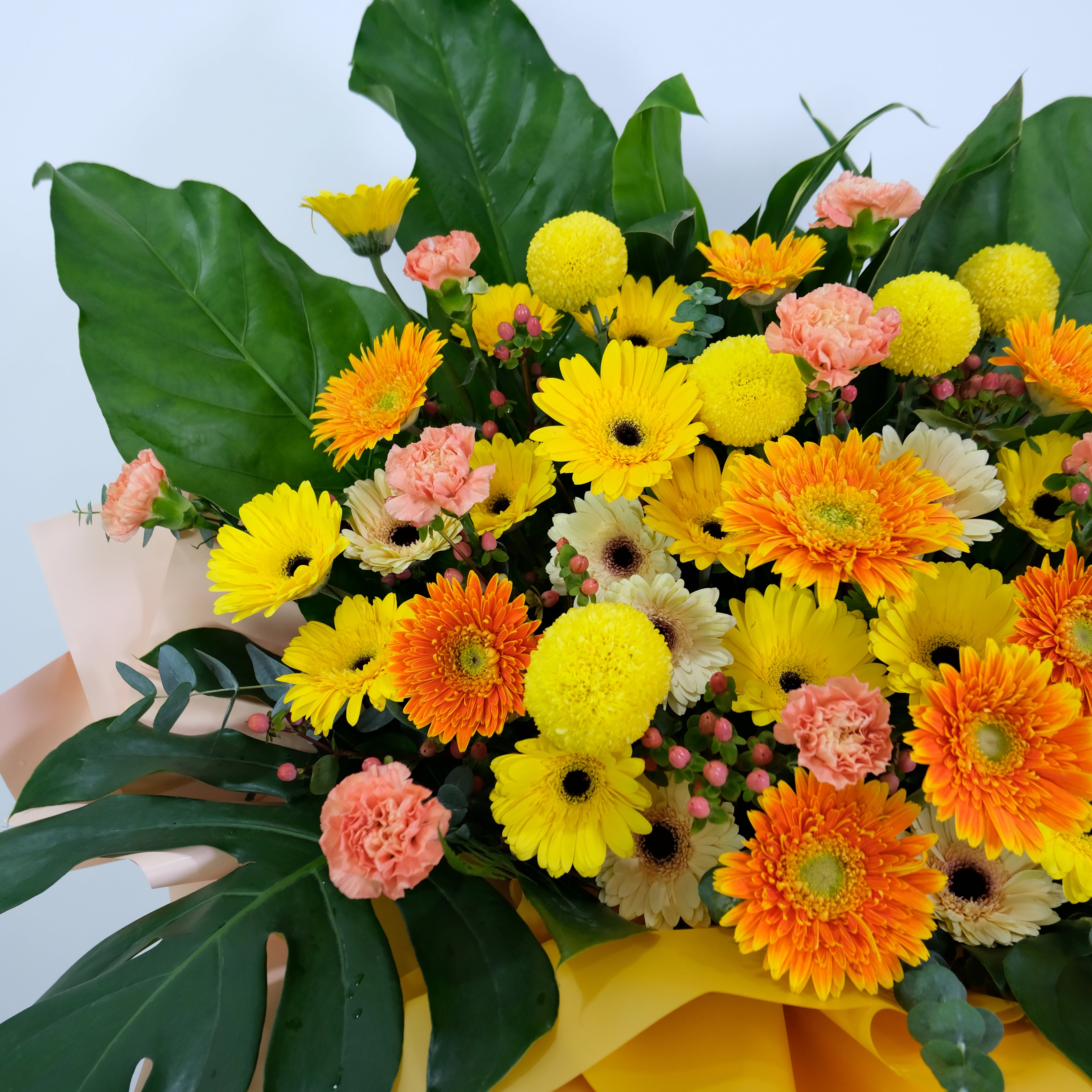 Bouquet of flowers with yellow, orange, and pink flowers, and green leaves on a light blue background.