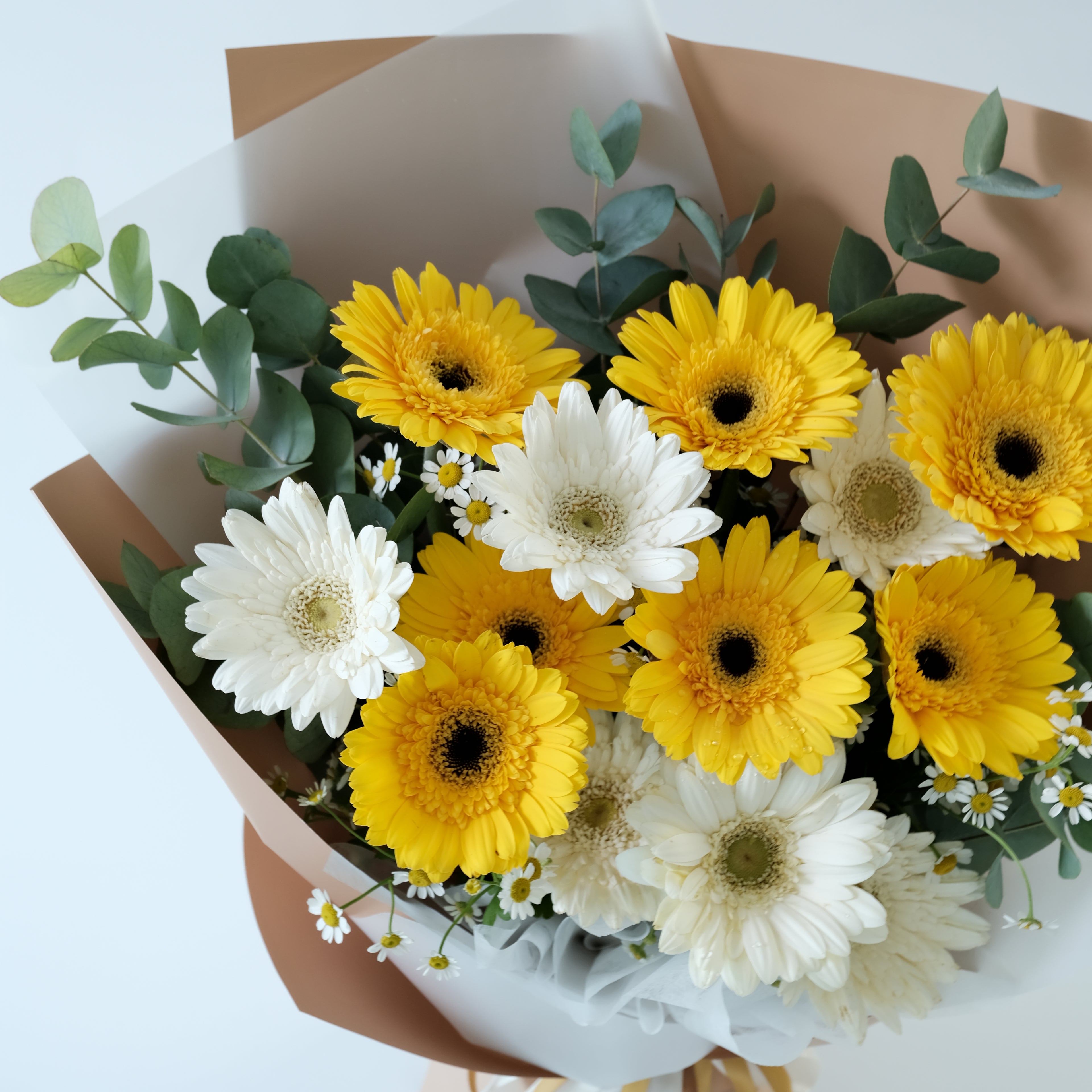 Bouquet of yellow and white flowers with greenery on a light background