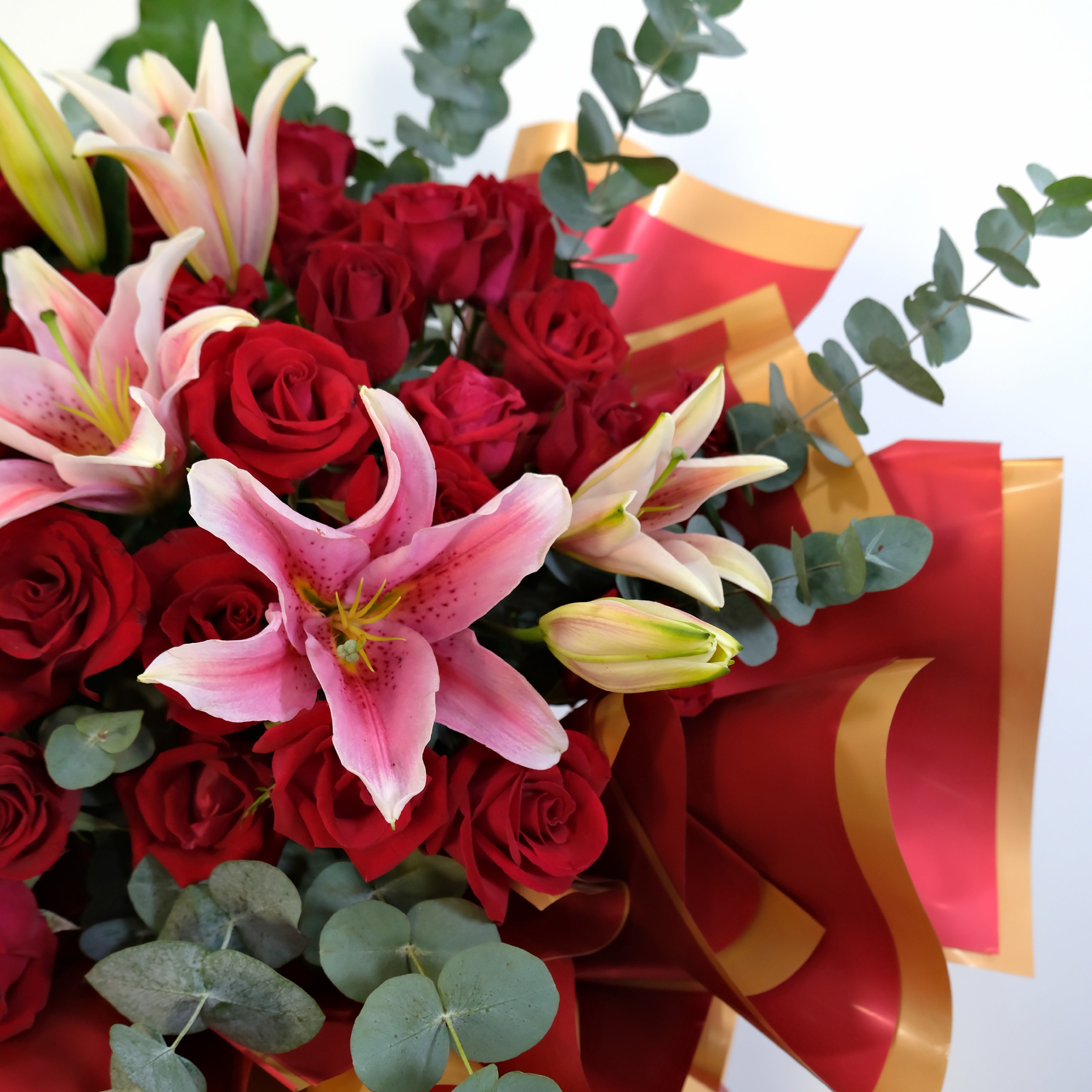Bouquet of red roses and pink lilies with a gold ribbon on a light gray background
