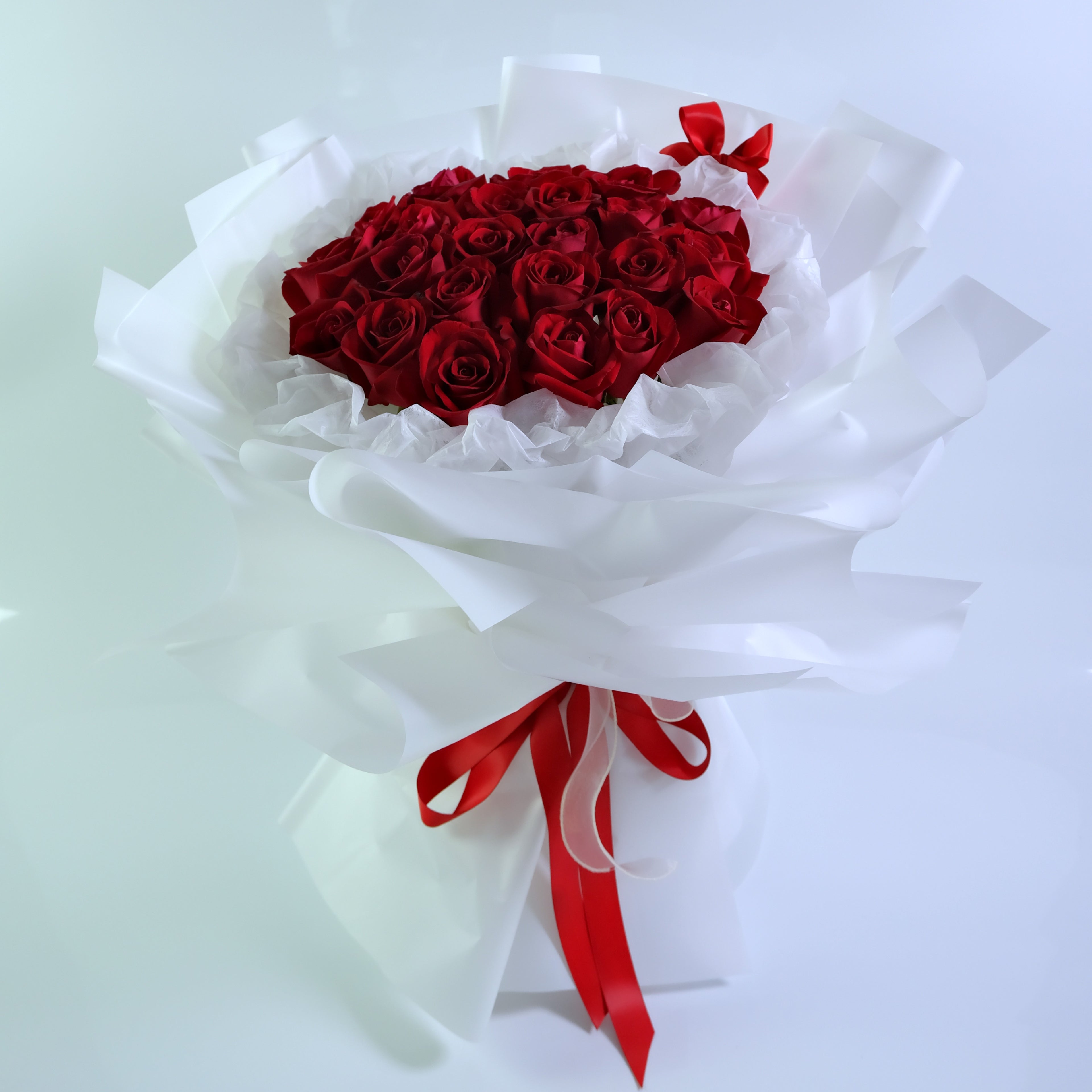Bouquet of red roses wrapped in white paper with a red ribbon on a light gray background