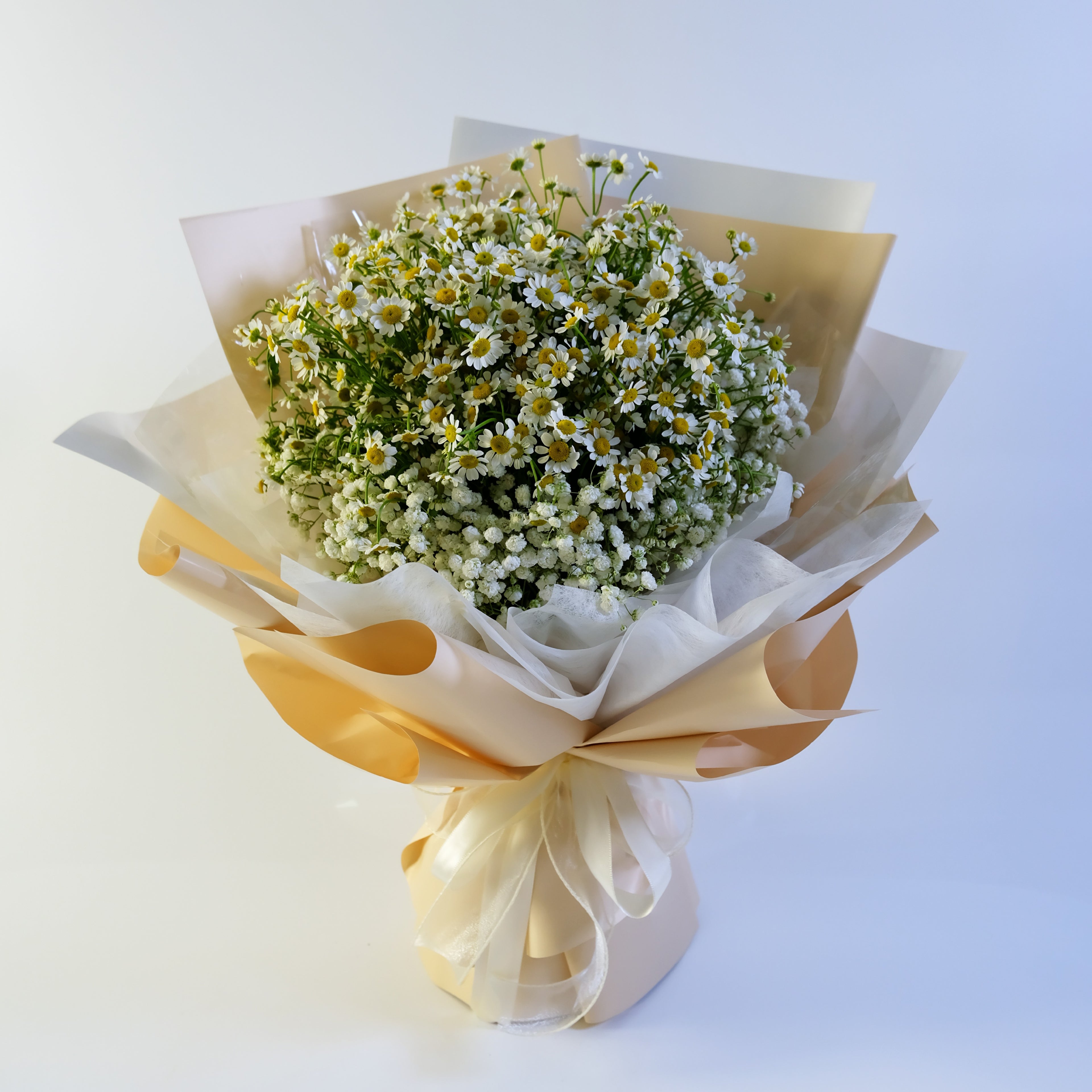Bouquet of white flowers with greenery wrapped in white paper and a yellow ribbon on a light blue background