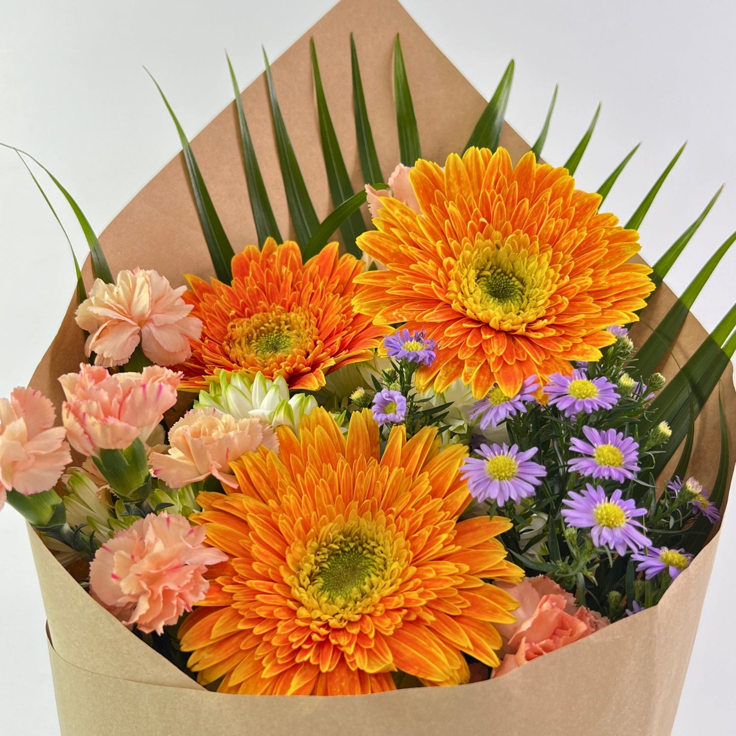 Bouquet of flowers with orange and pink flowers wrapped in brown paper on a white background