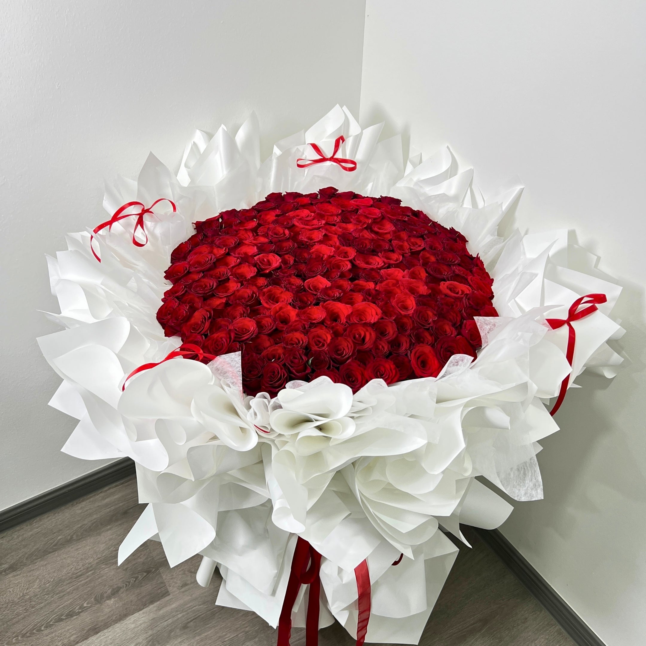 199 stems of red roses wrapped in white paper with red ribbons on a light gray background