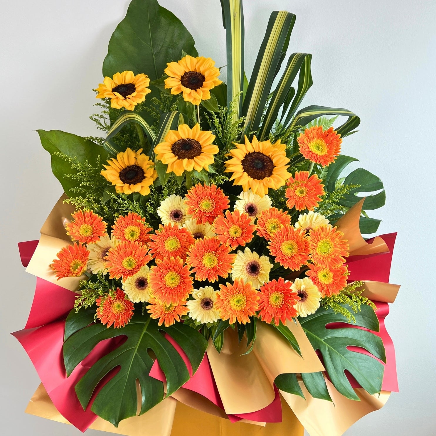 Bouquet of sunflowers and orange gerberas with green leaves on a light gray background