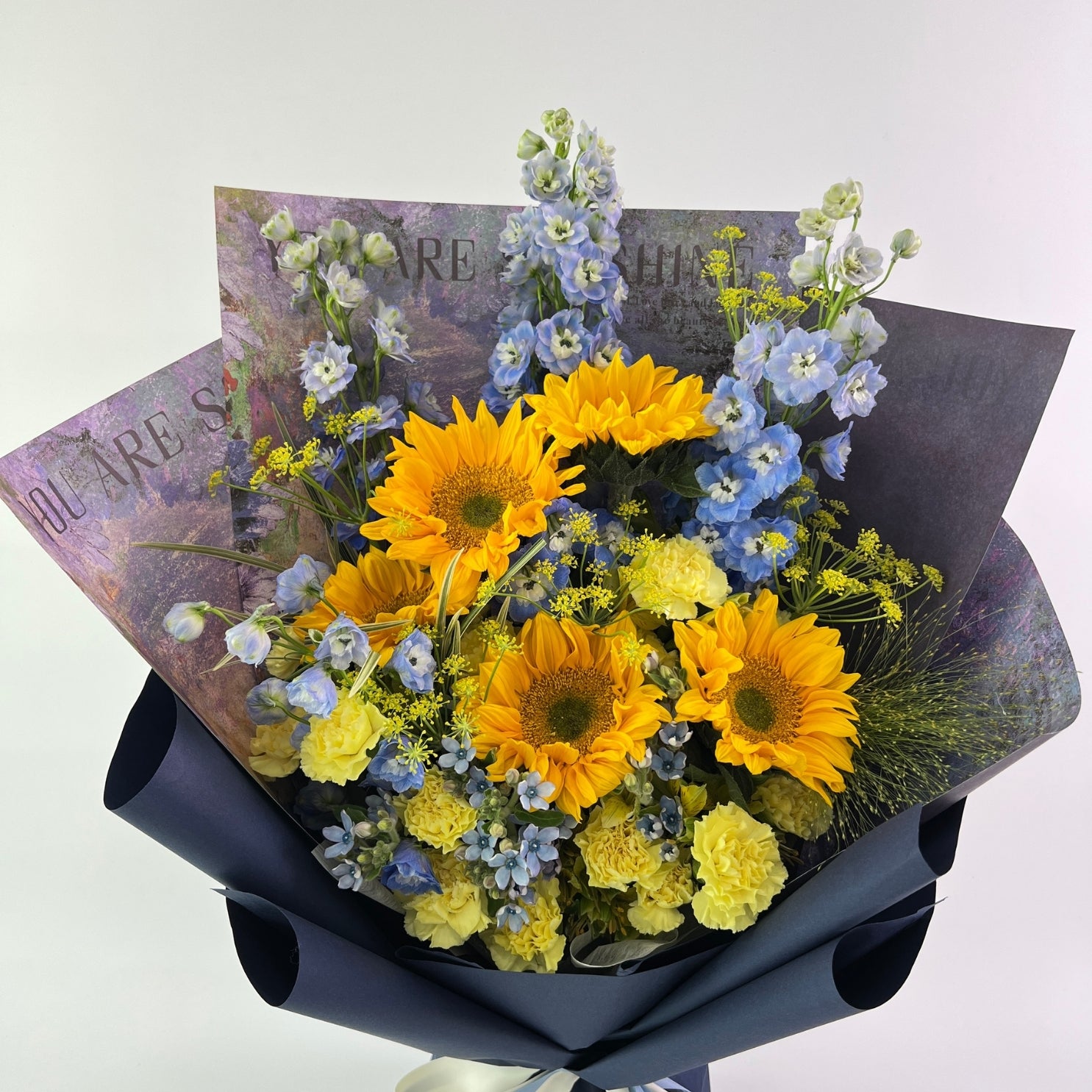 Bouquet of yellow and blue flowers wrapped in black paper with a message card.