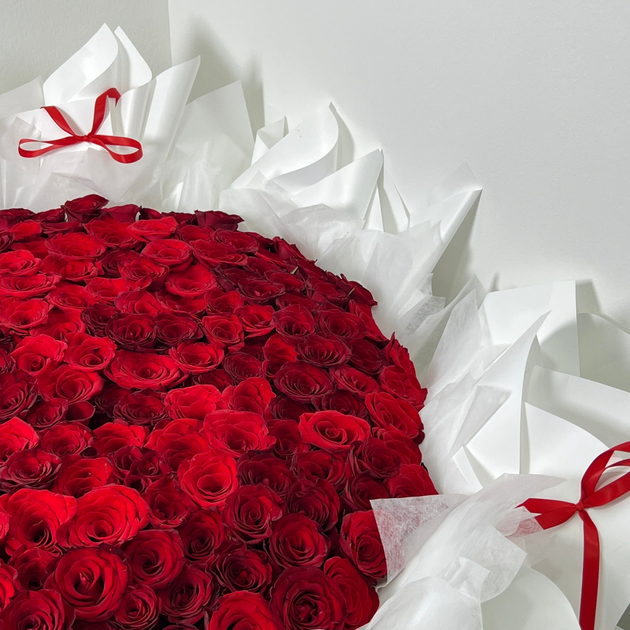 199 stems of red roses wrapped in white paper with red ribbons on a light gray background