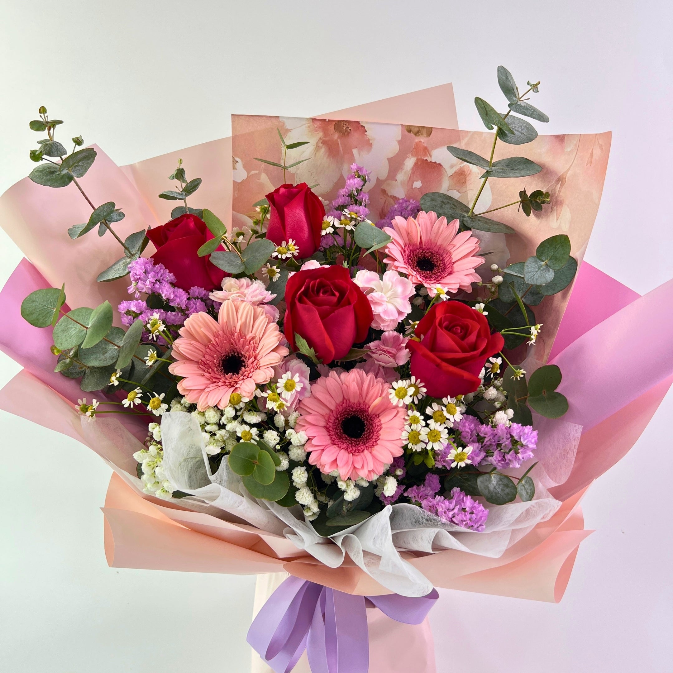 Bouquet of red and pink flowers with greenery on a light background