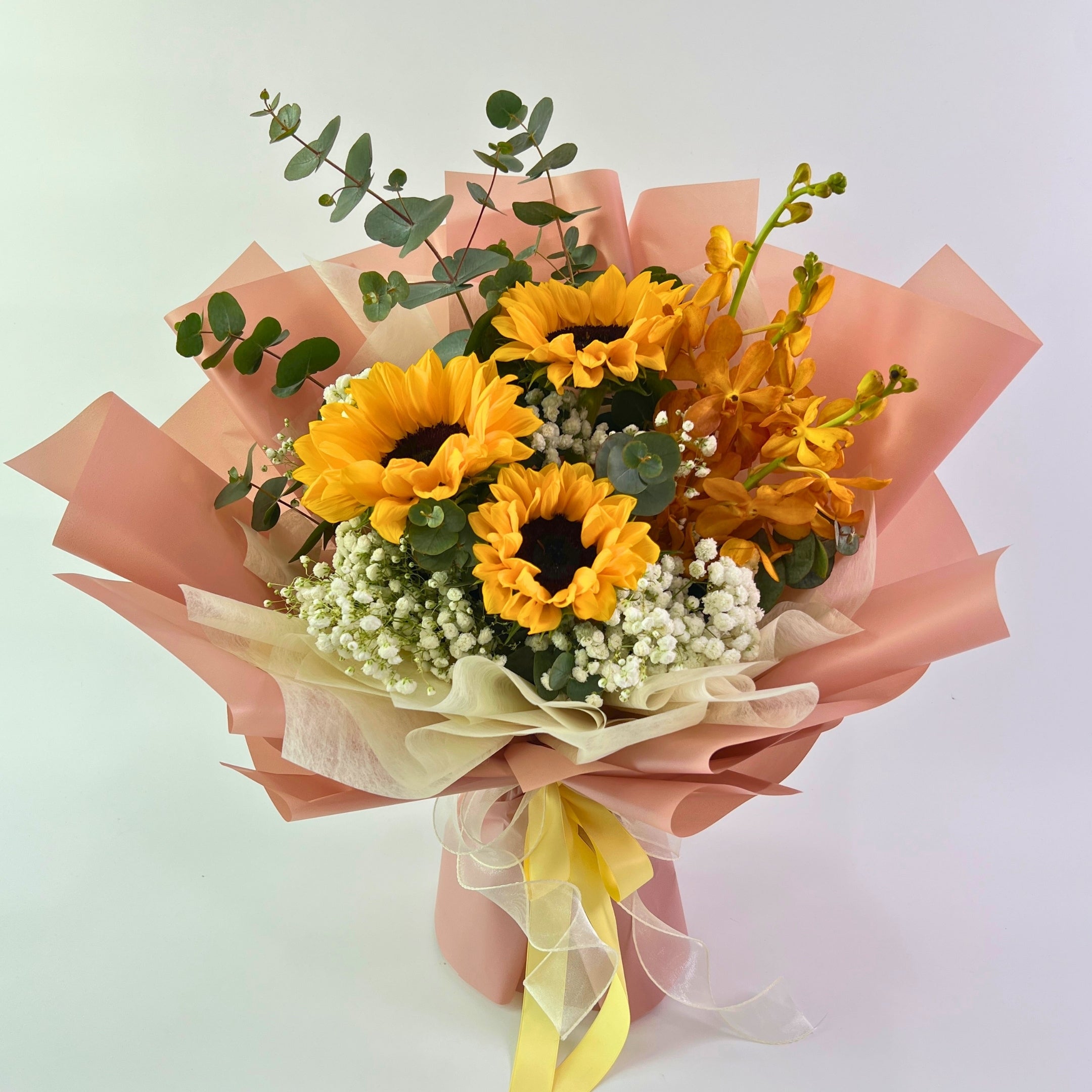 Bouquet of sunflowers and other flowers wrapped in pink paper with a yellow ribbon on a light background
