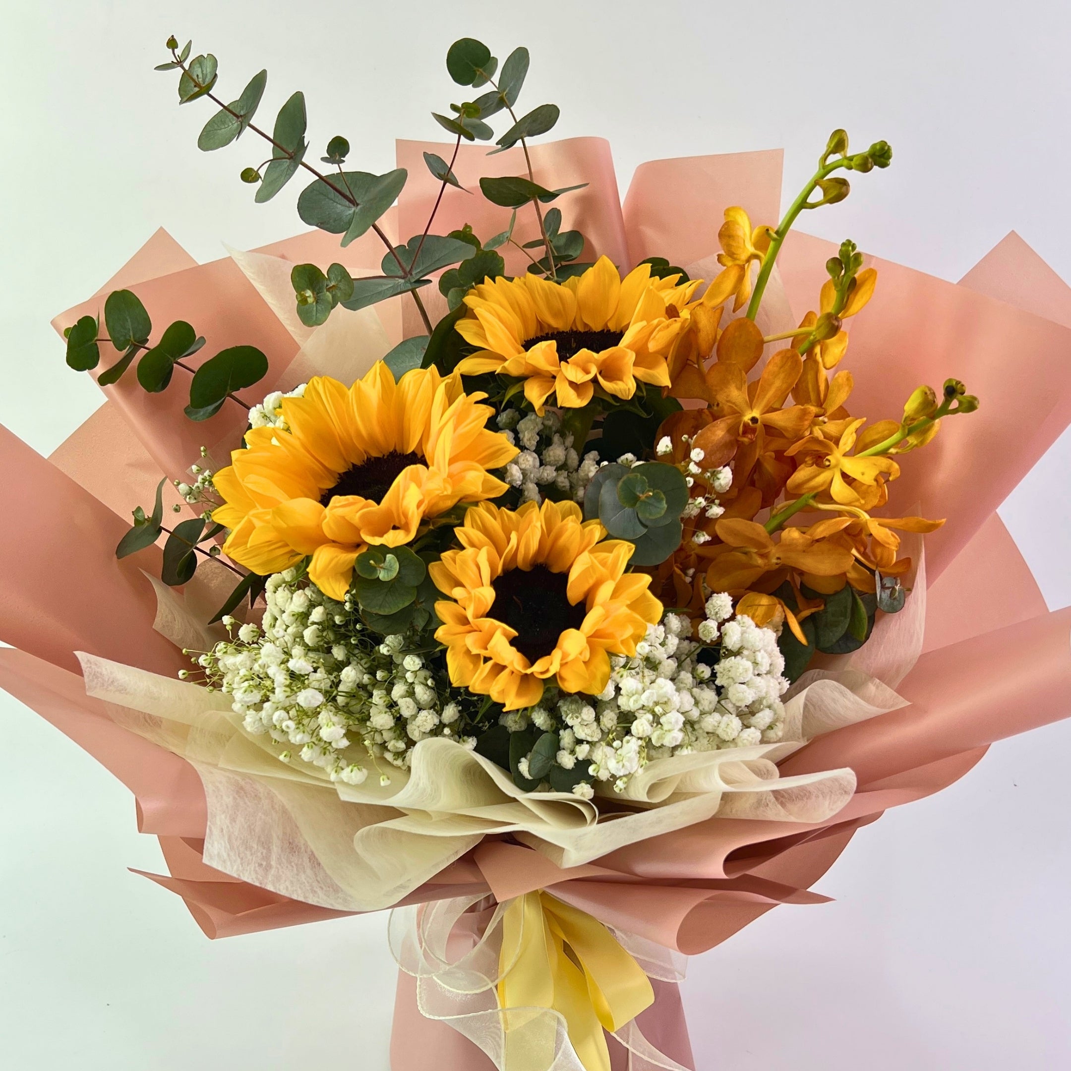Bouquet of sunflowers and other flowers with pink and beige paper wrapping on a light background