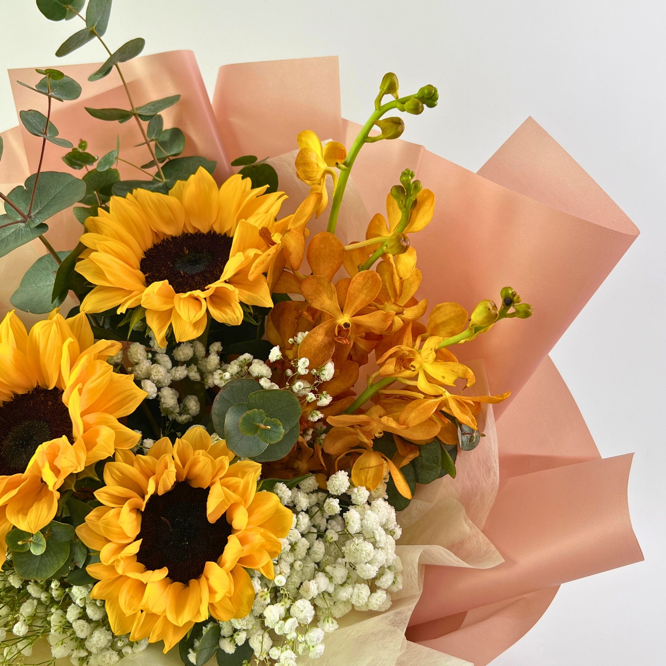 Bouquet of sunflowers and orchids wrapped in pink paper on a light background