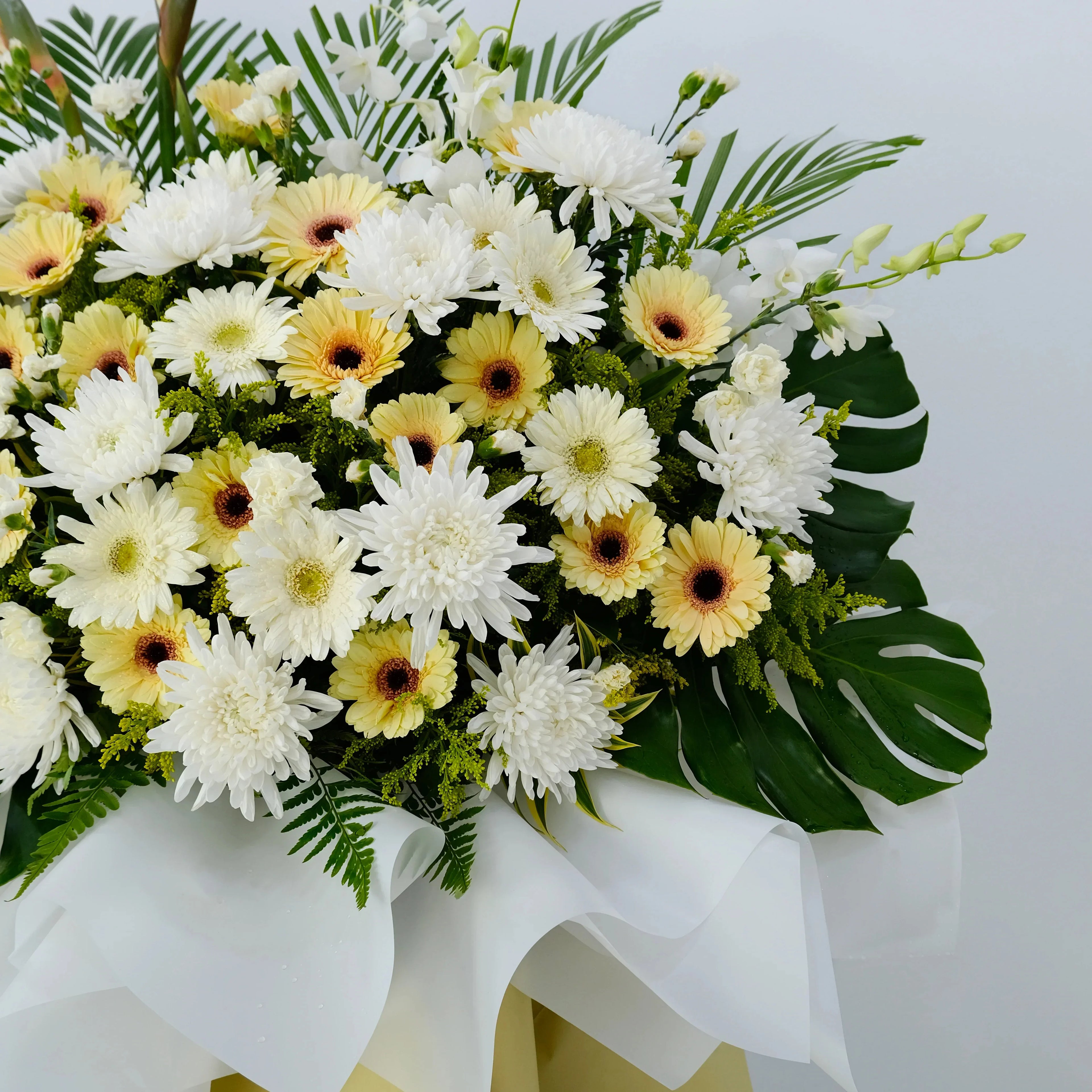 White and yellow gerbera daisy and chrysanthemum flower arrangement with green leaves