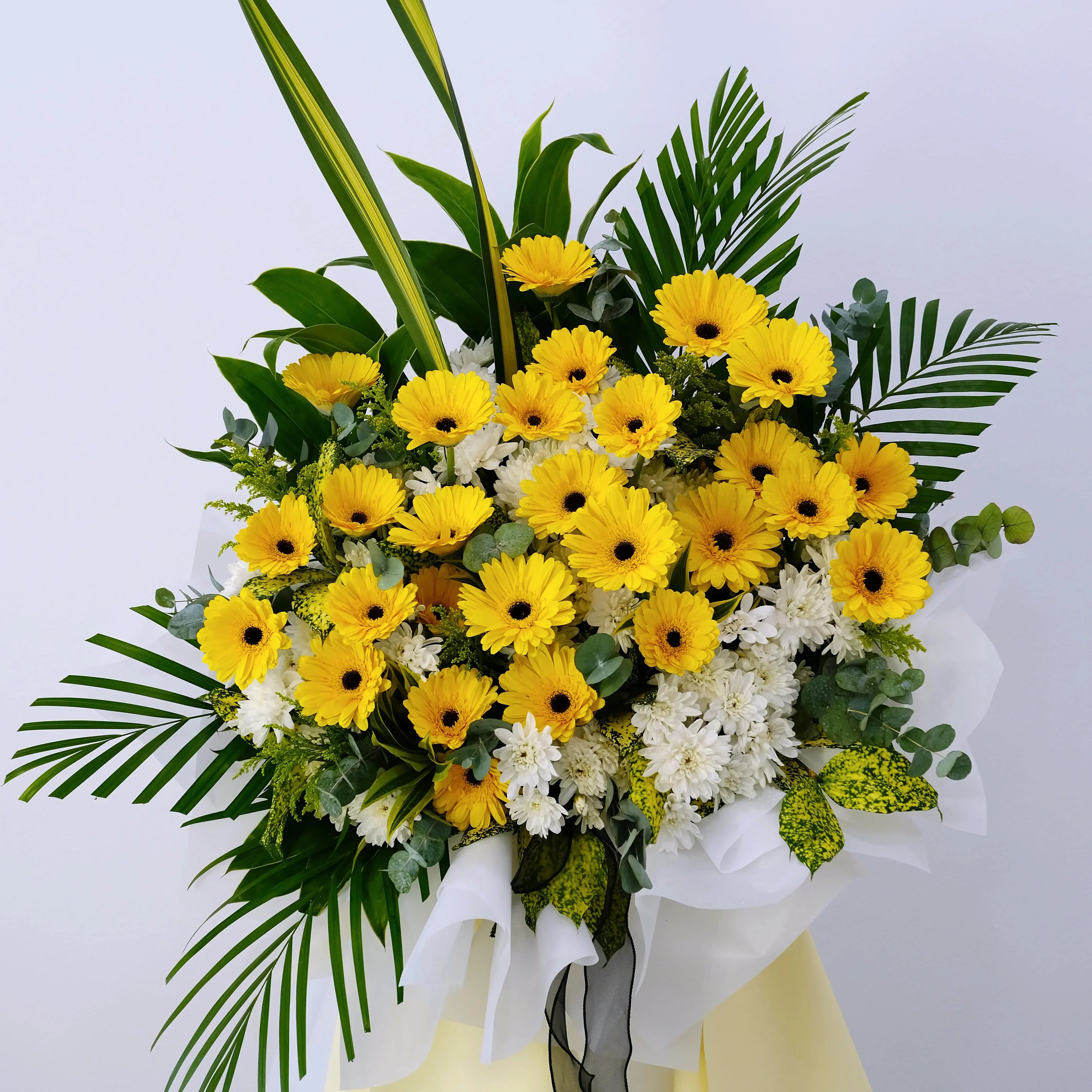 Bouquet of yellow gerbera daisies, white chrysanthemums, palm leaves, and green foliage