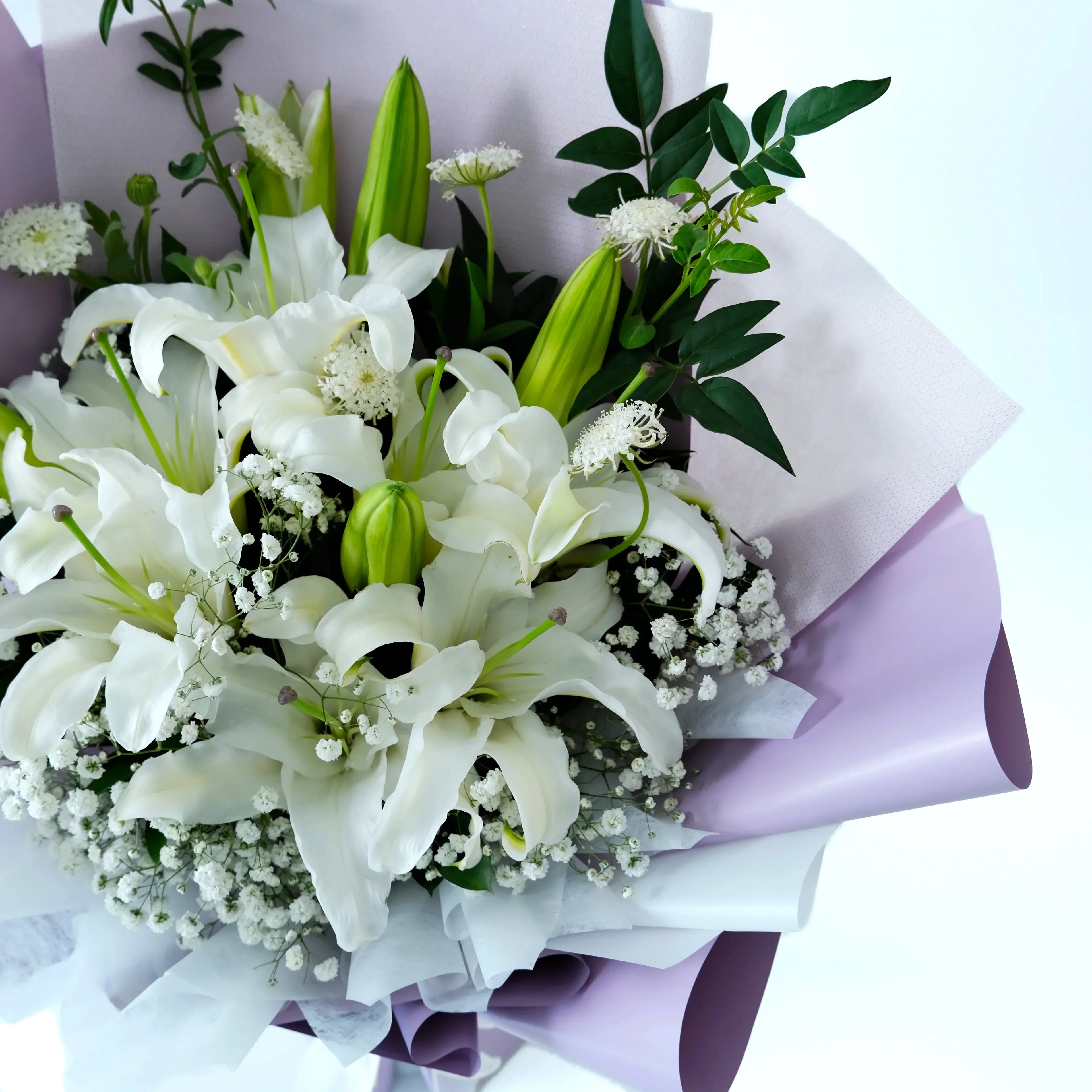 Bouquet of white lilies and greenery with a light purple wrap on a white background