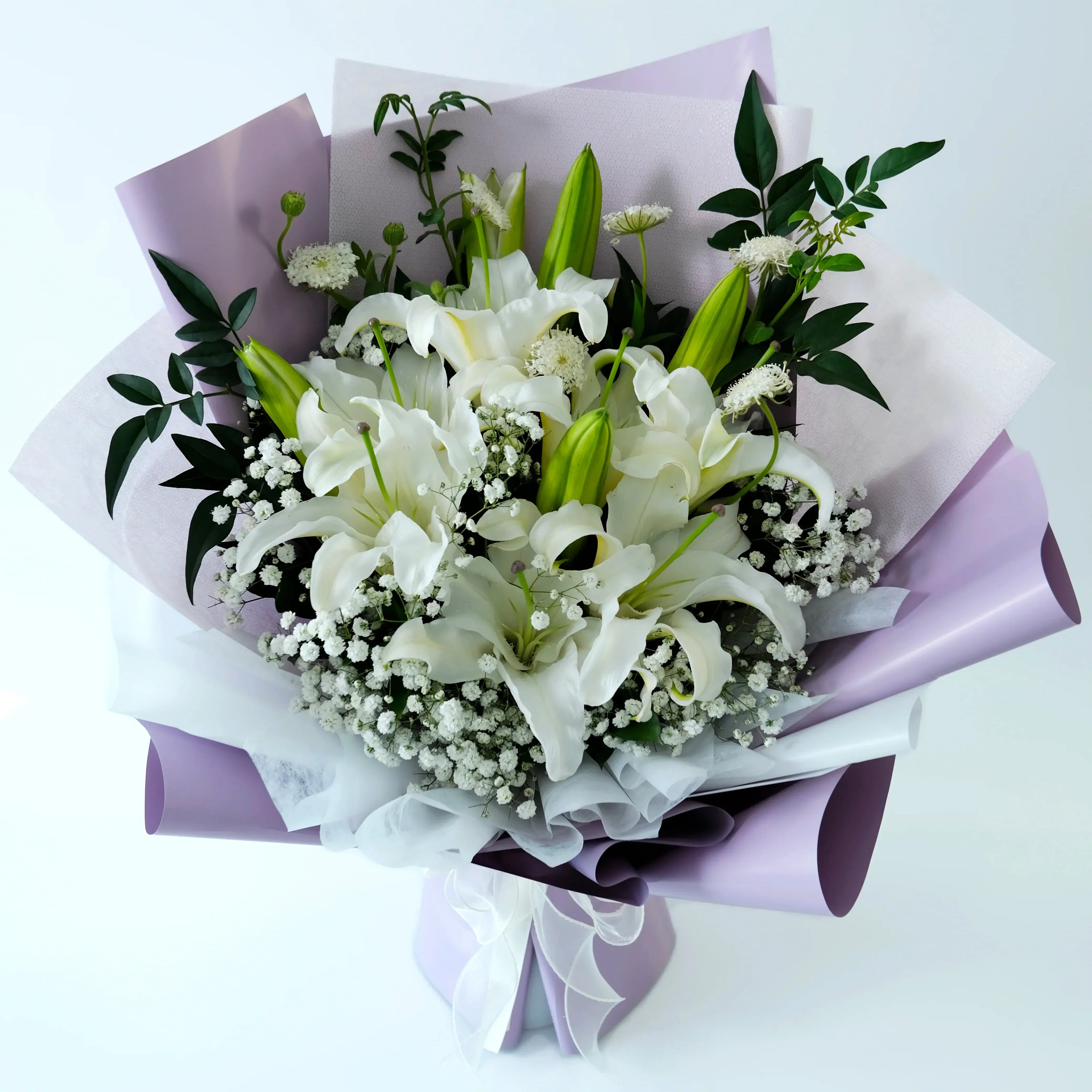 Bouquet of white lilies and greenery wrapped in purple paper on a white background