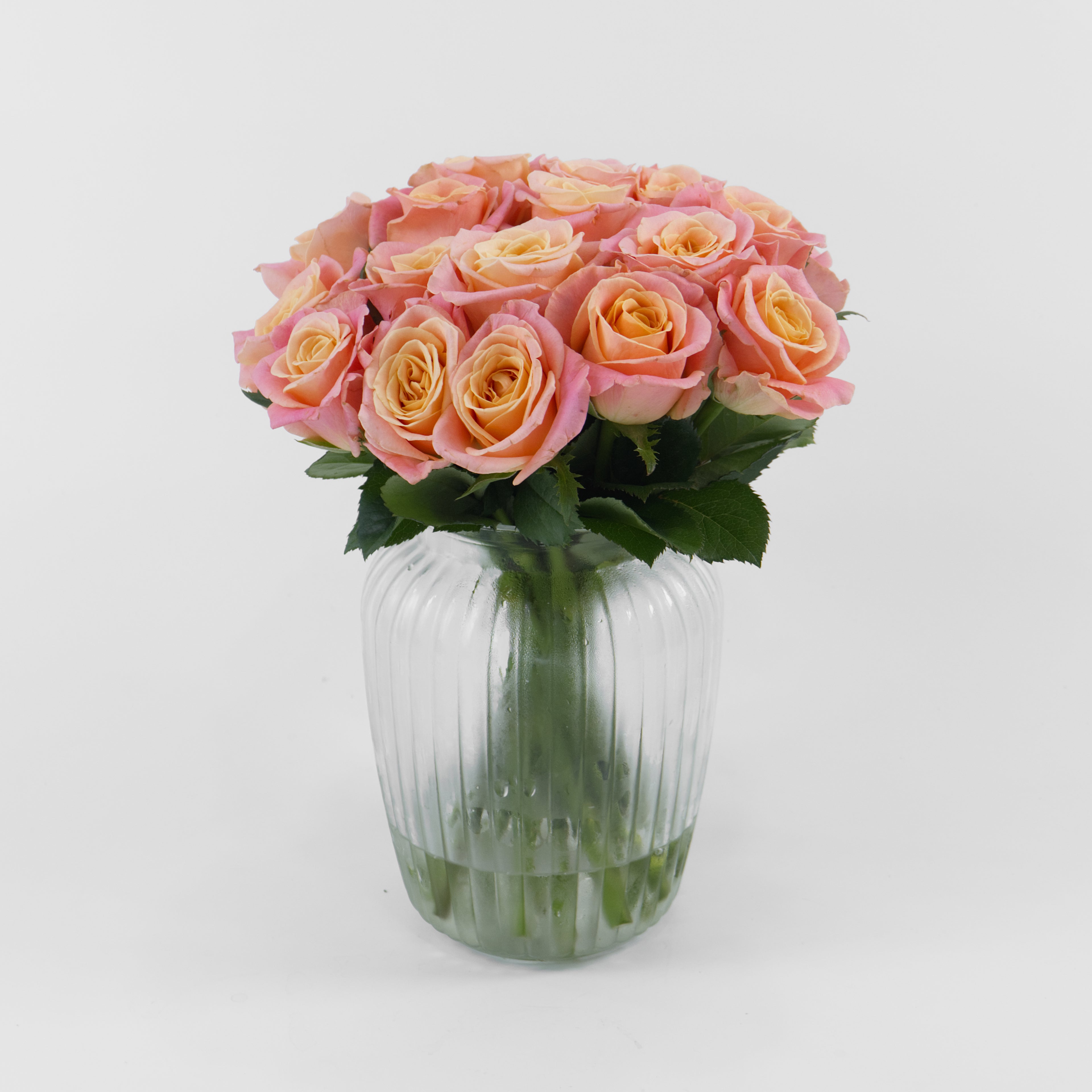 Bouquet of pink and peach roses in a clear glass vase on a white background