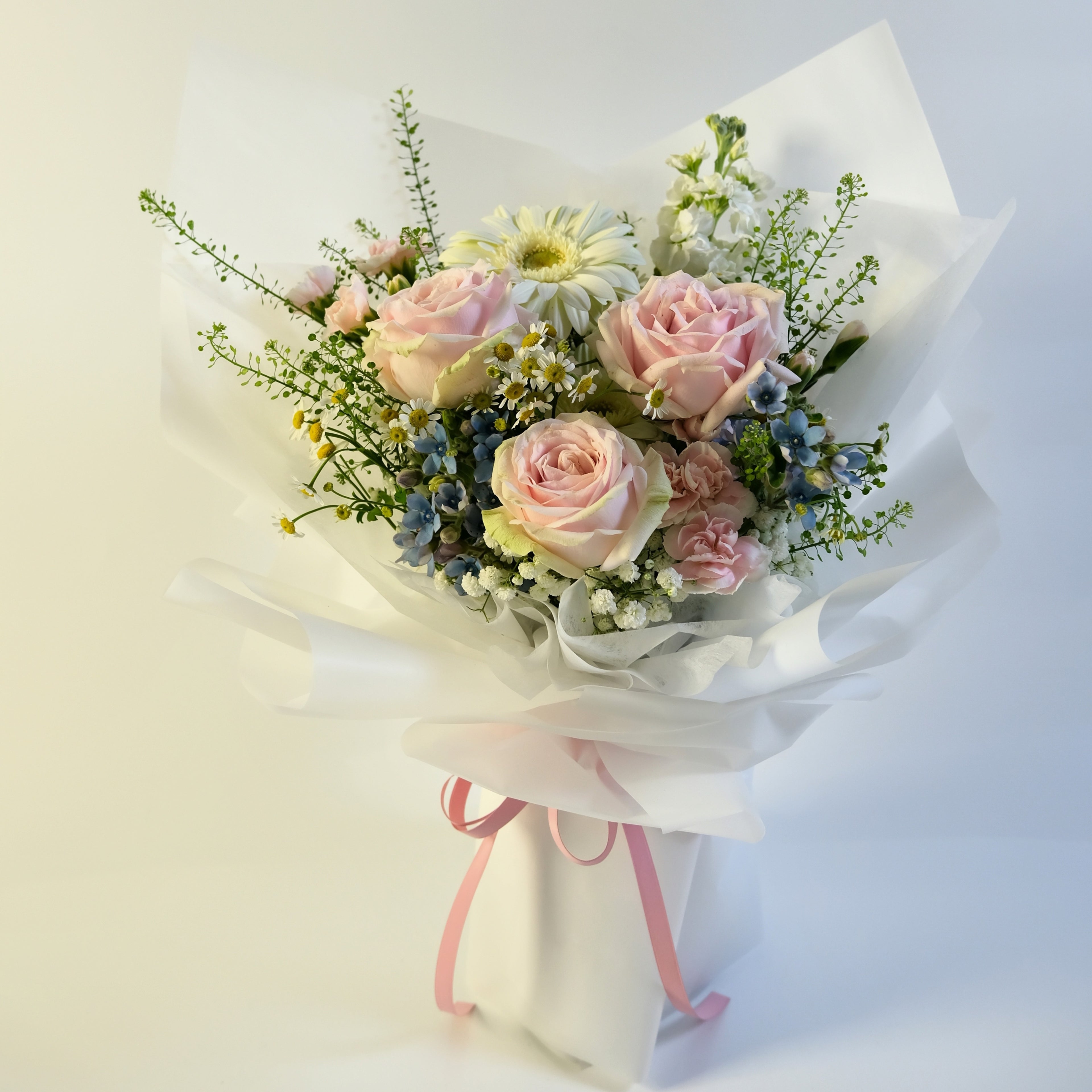 Bouquet of pink roses and greenery with a white ribbon on a light background