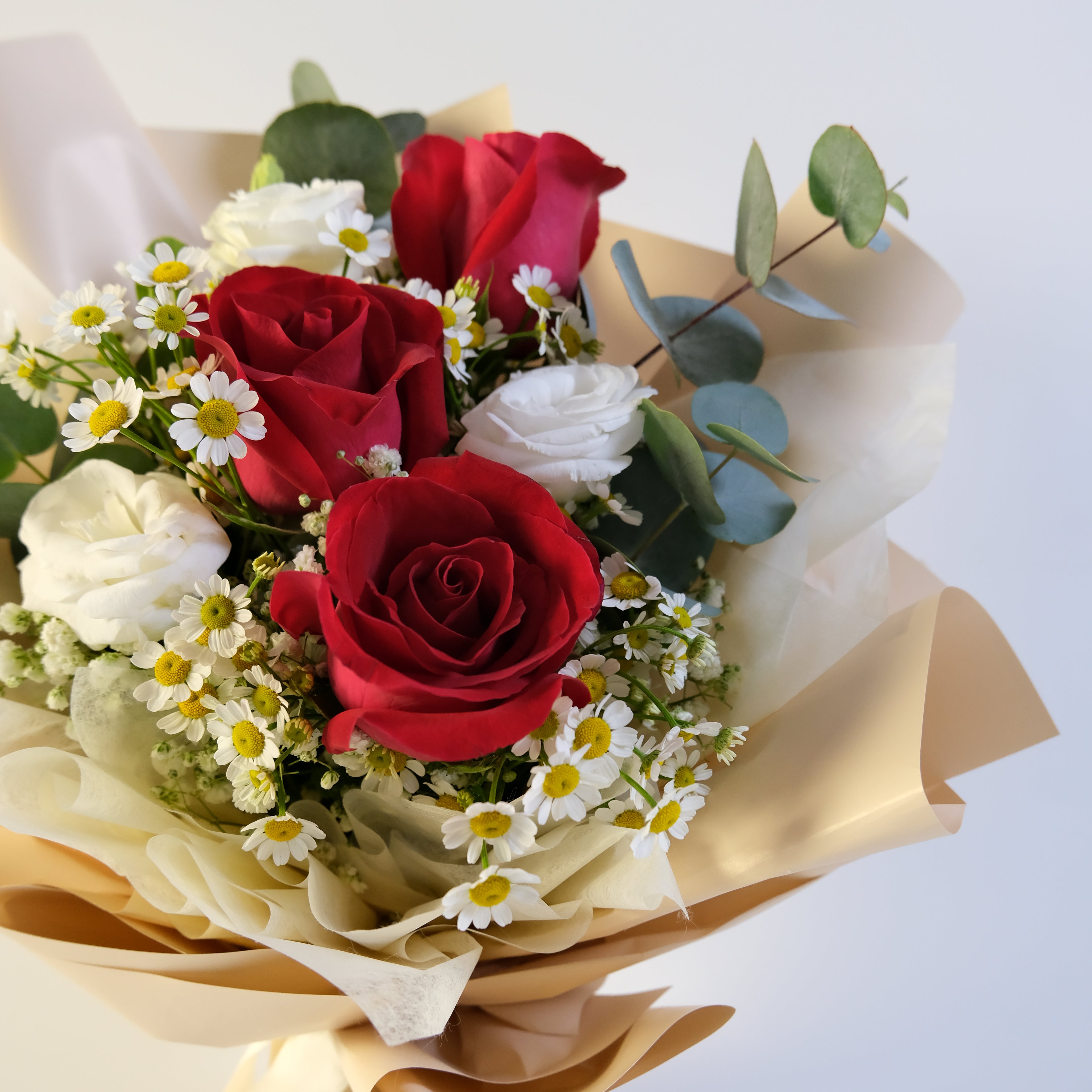 Bouquet of red, white, and pink roses with greenery on a light background