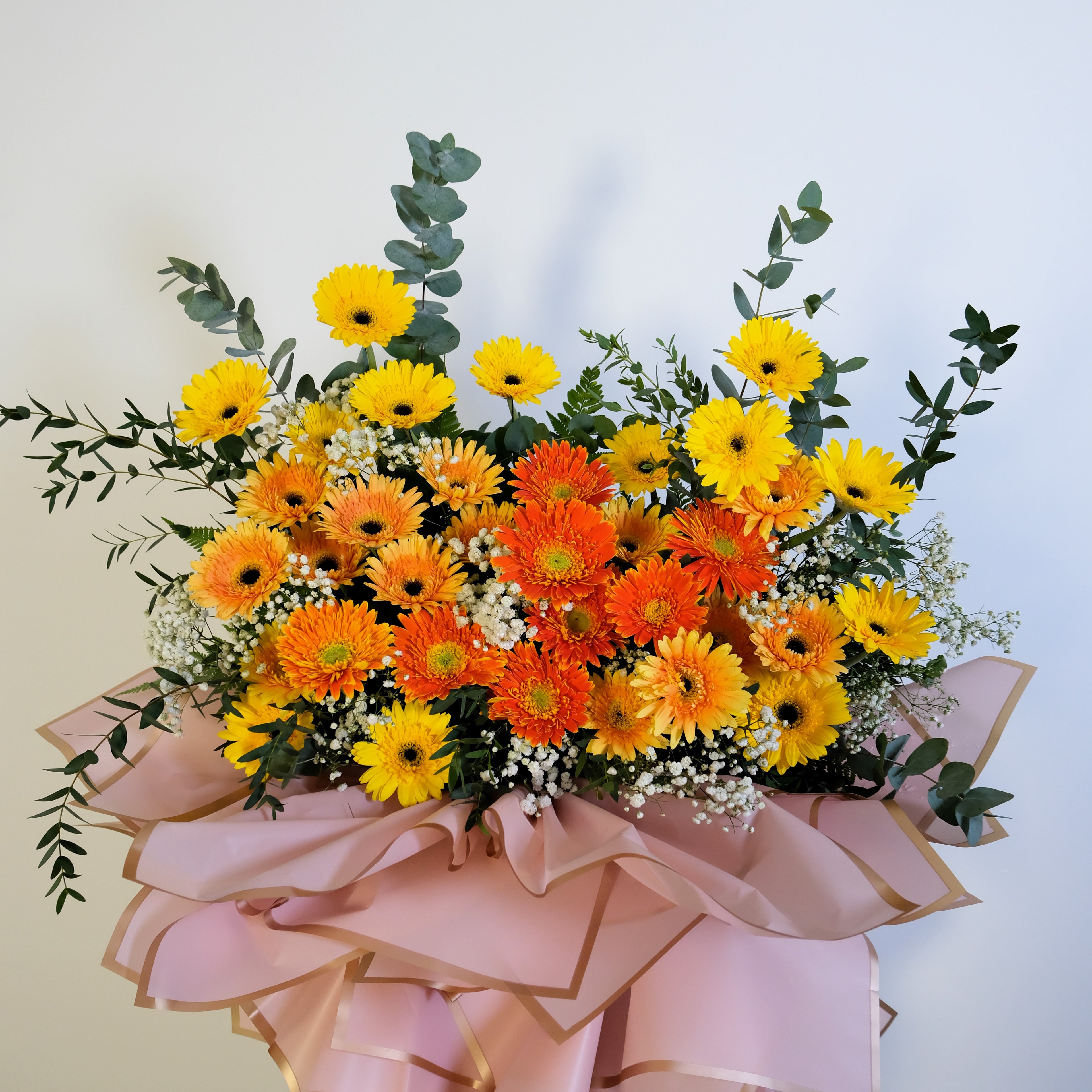 opening flower stand of yellow and orange flowers with greenery on a light background