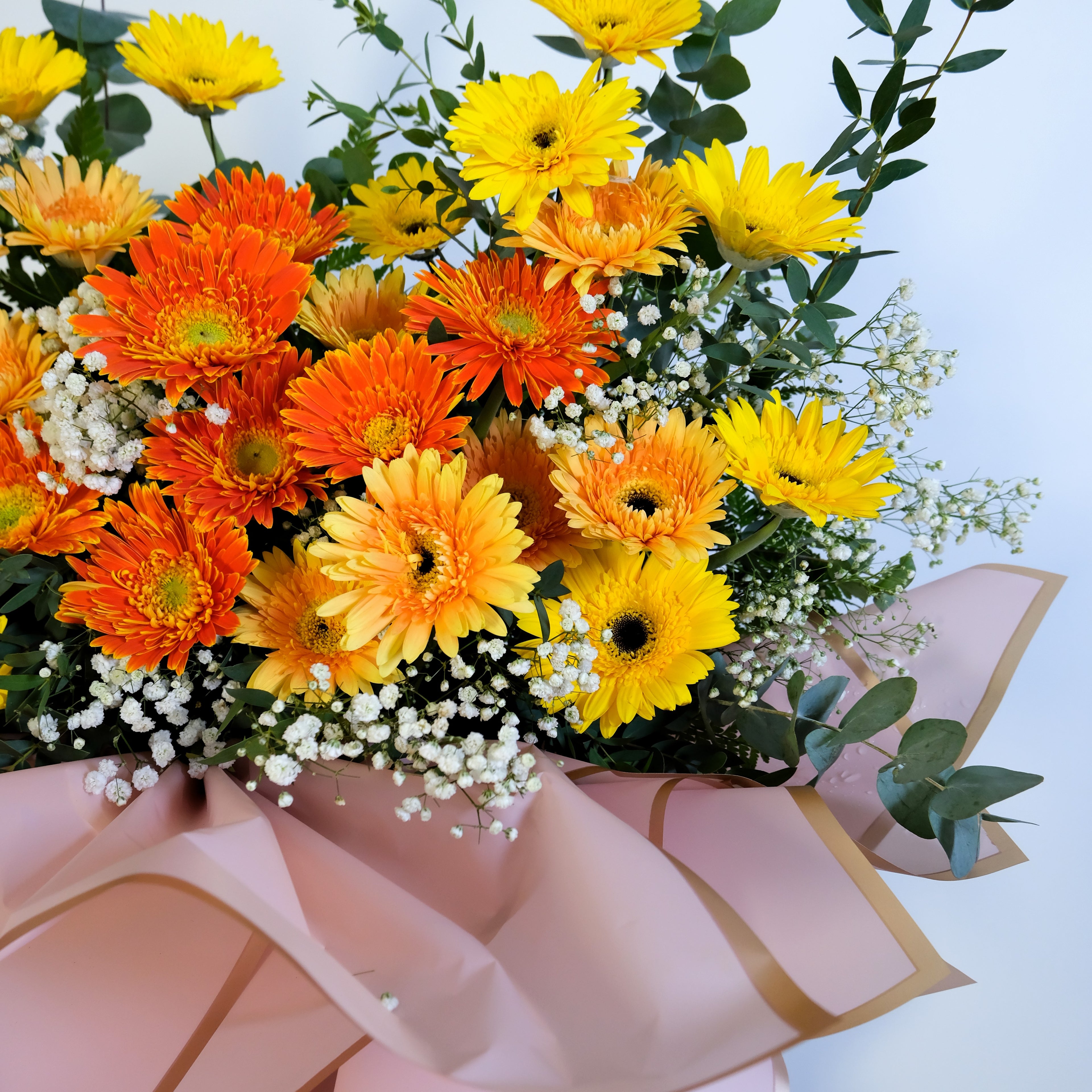 flower stand of orange and yellow flowers with greenery on a light blue background
