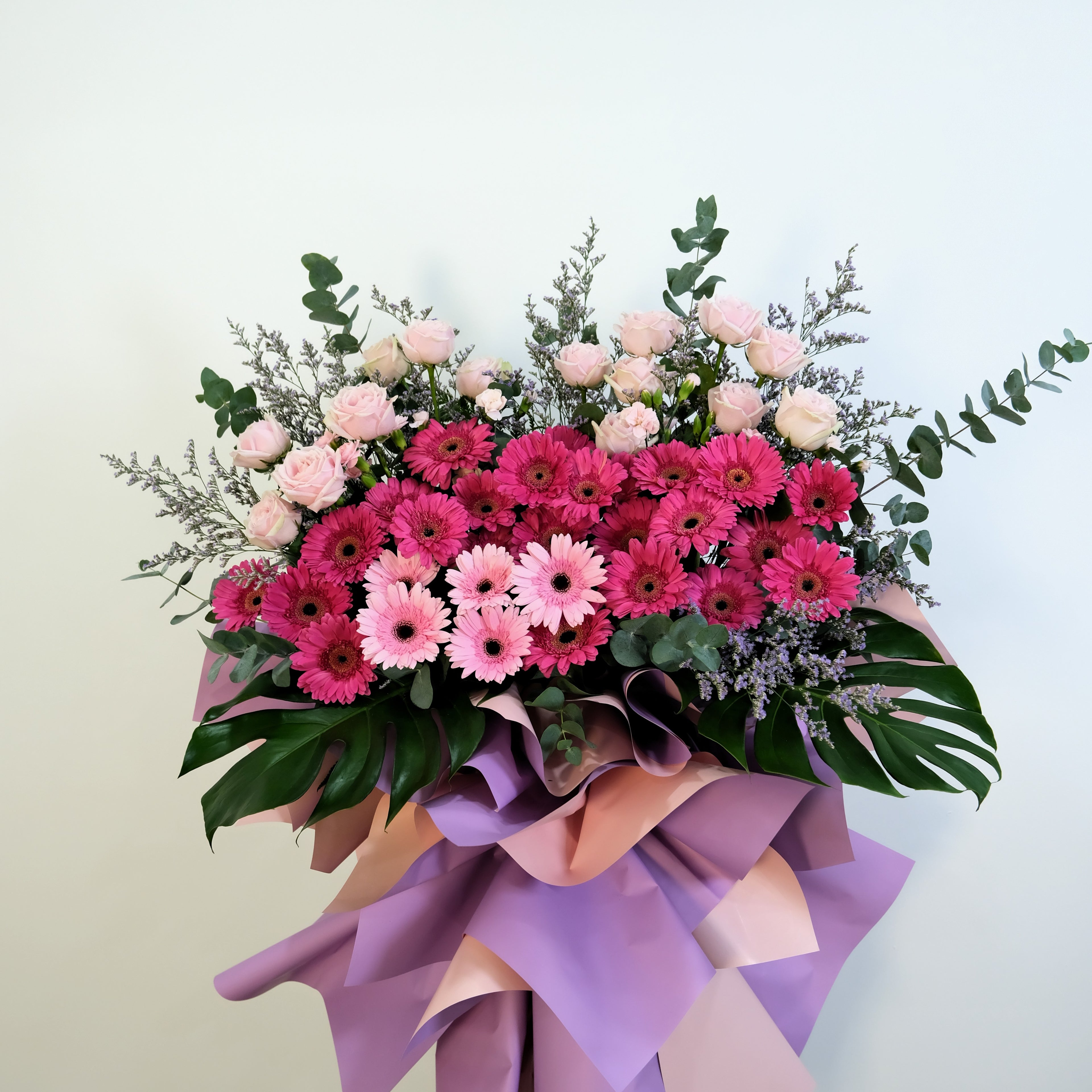 flower stand of pink and green flowers with a purple ribbon on a light background