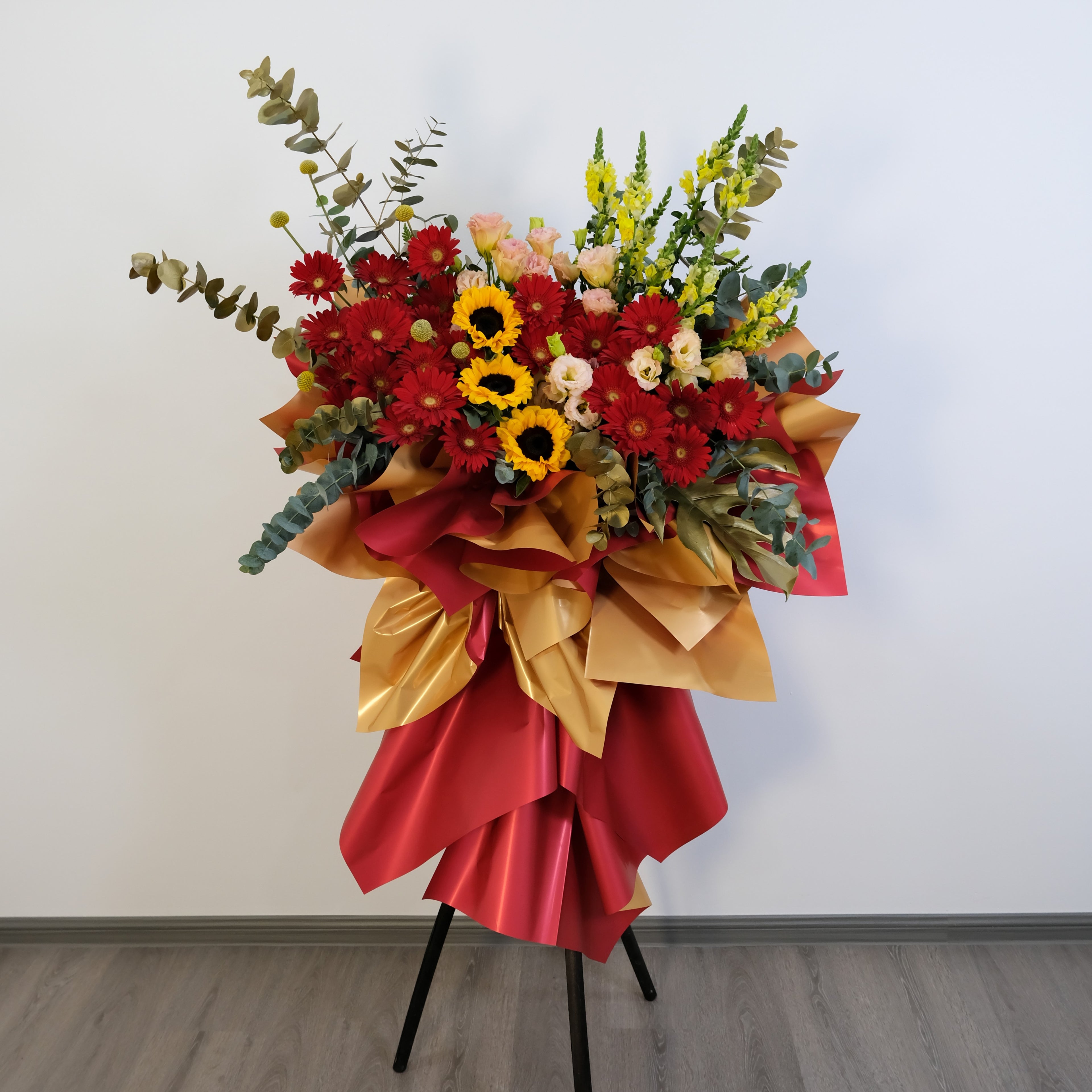 Colorful flower stand with red, yellow, and green flowers on a stand against a white wall.