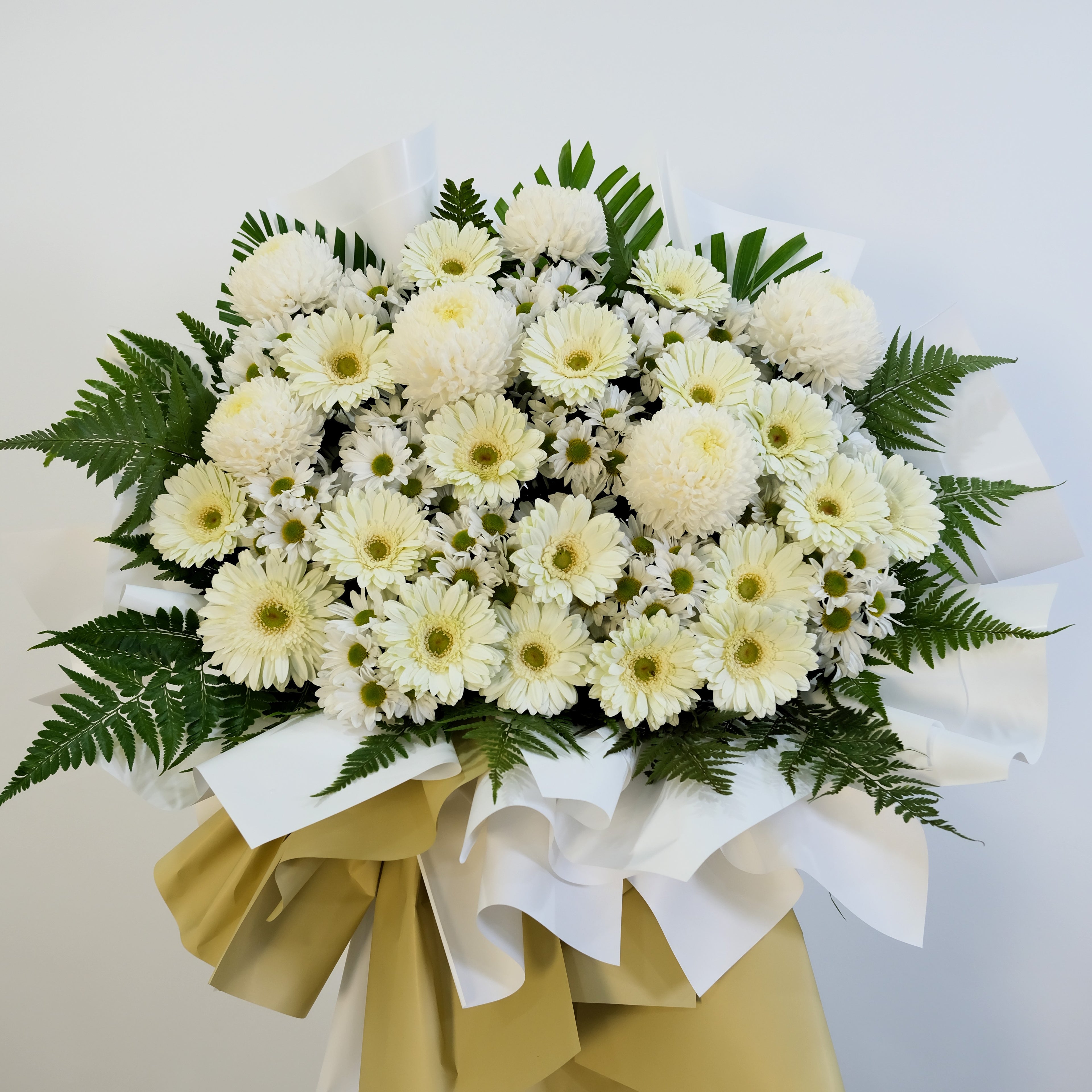 condolence flower stand of white and yellow flowers with green leaves on a light gray background