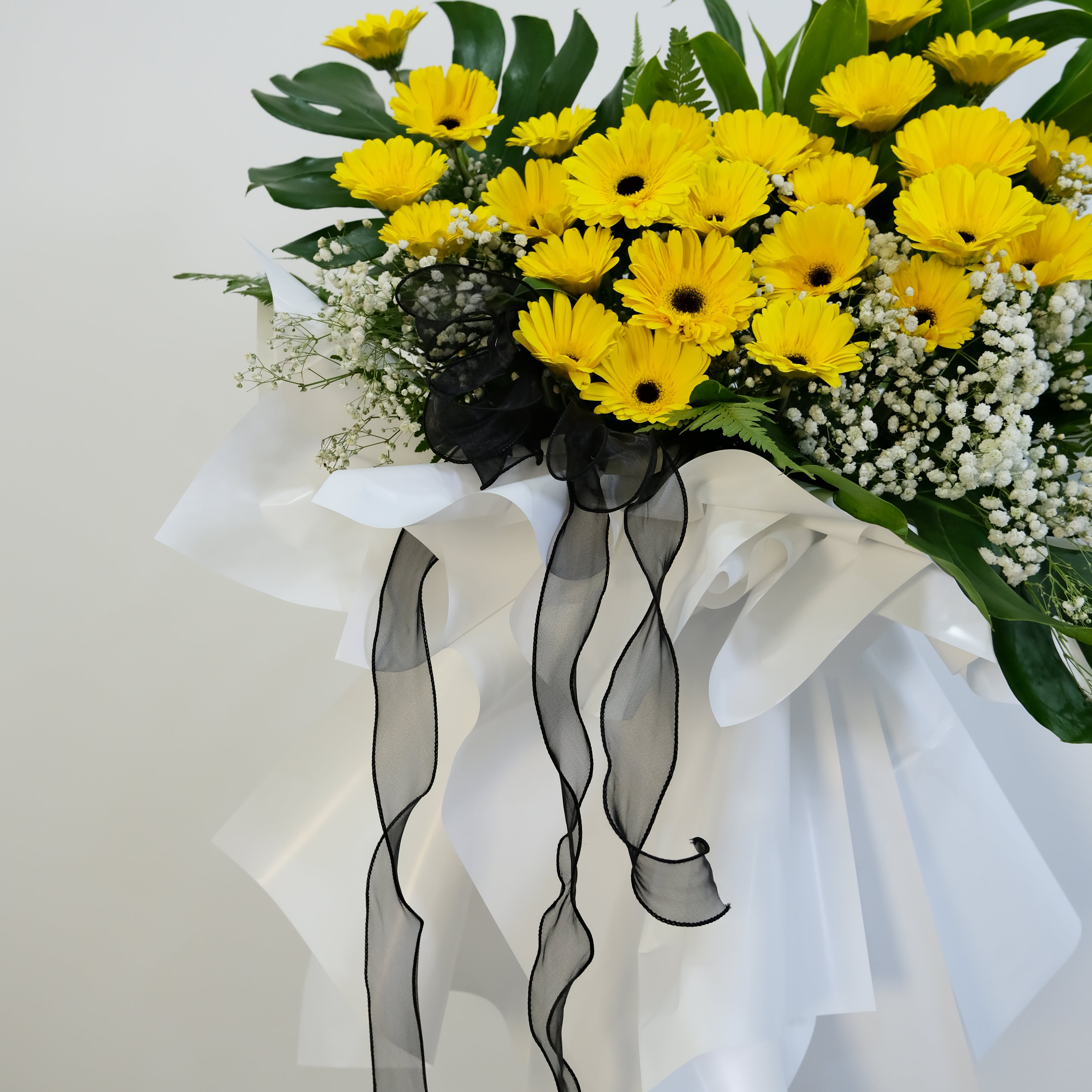 condolence Bouquet of yellow flowers with green leaves and black ribbons on a white background