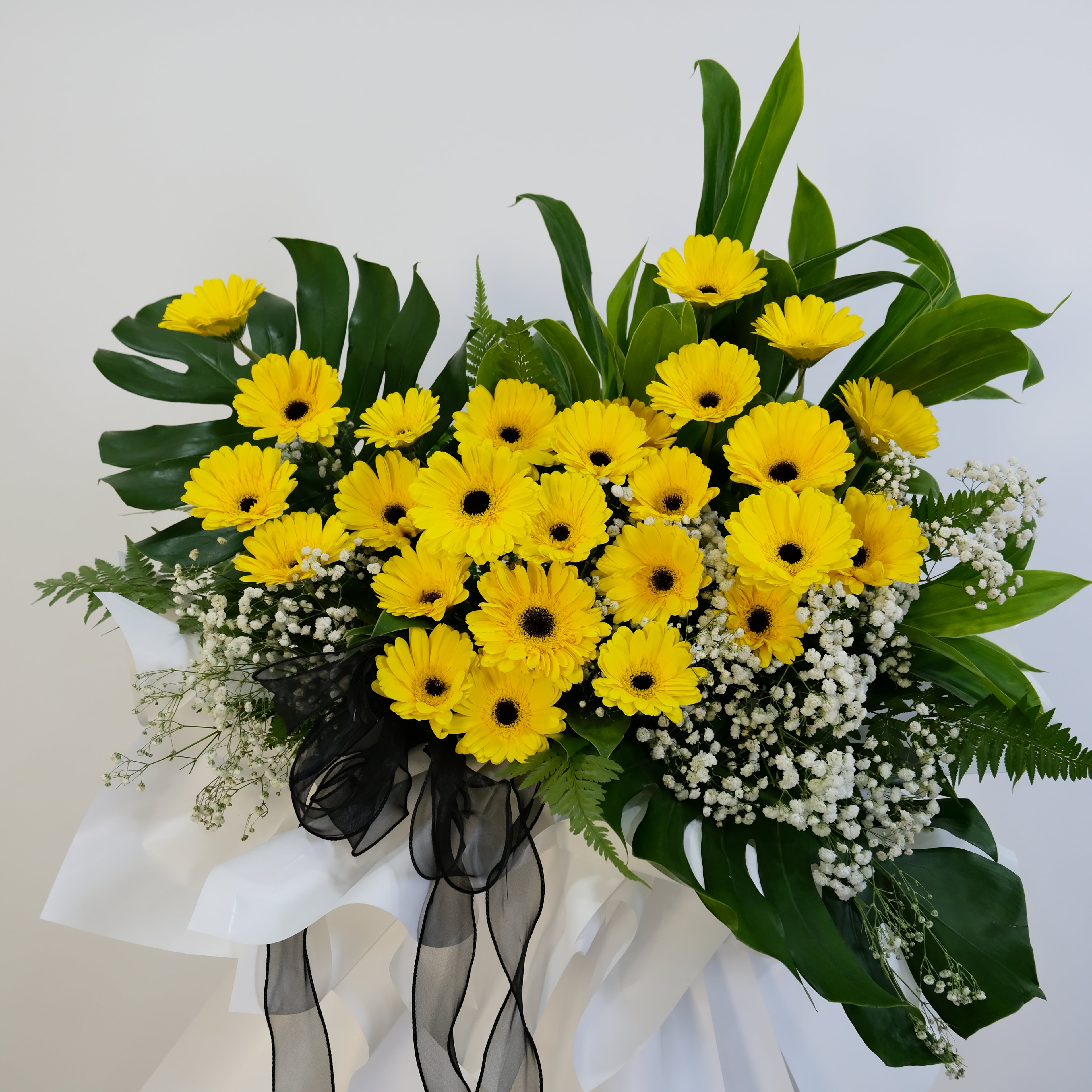 condolence flower stand of yellow flowers with green leaves and white accents on a light background