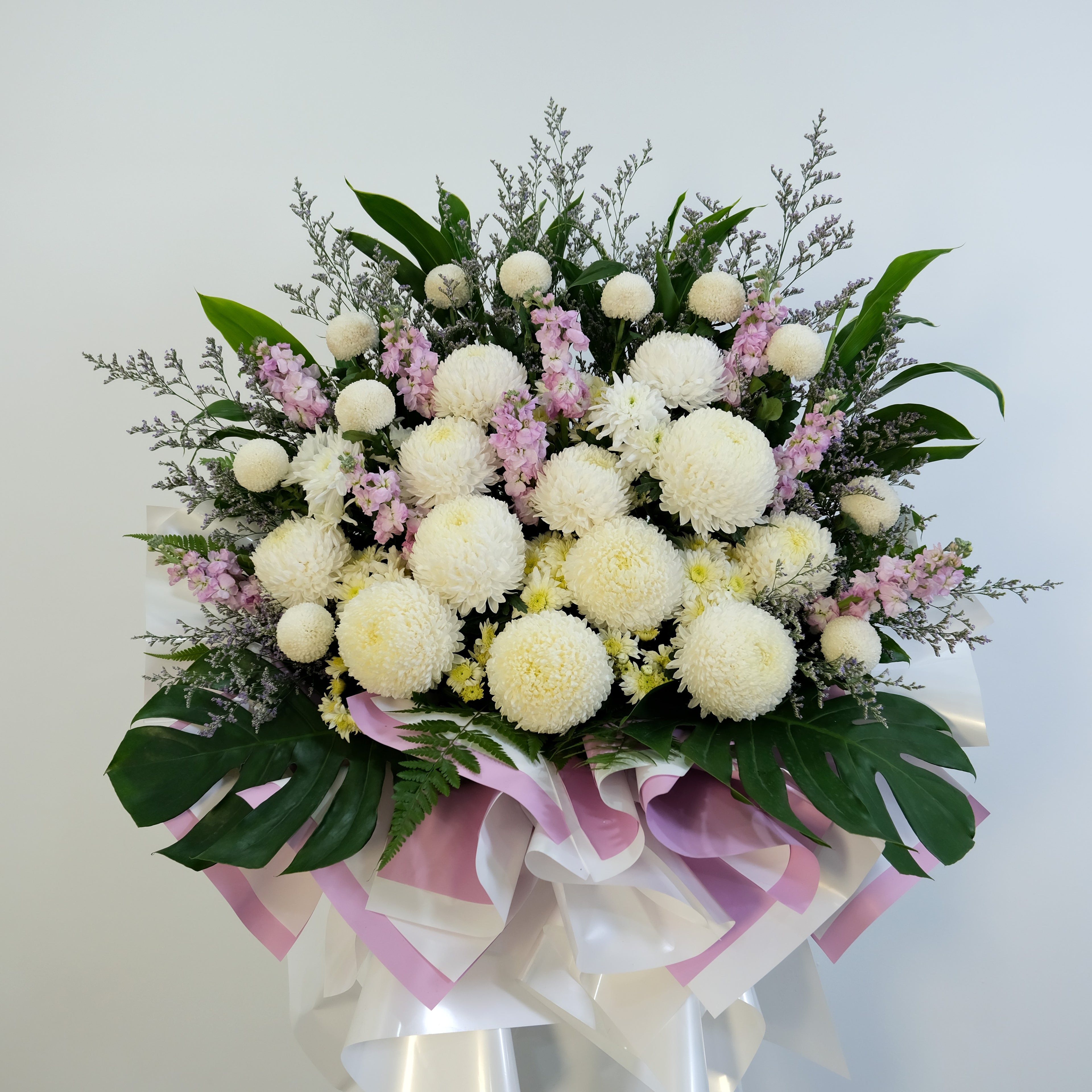 condolence flower stand of white and pink flowers with green leaves on a light gray background