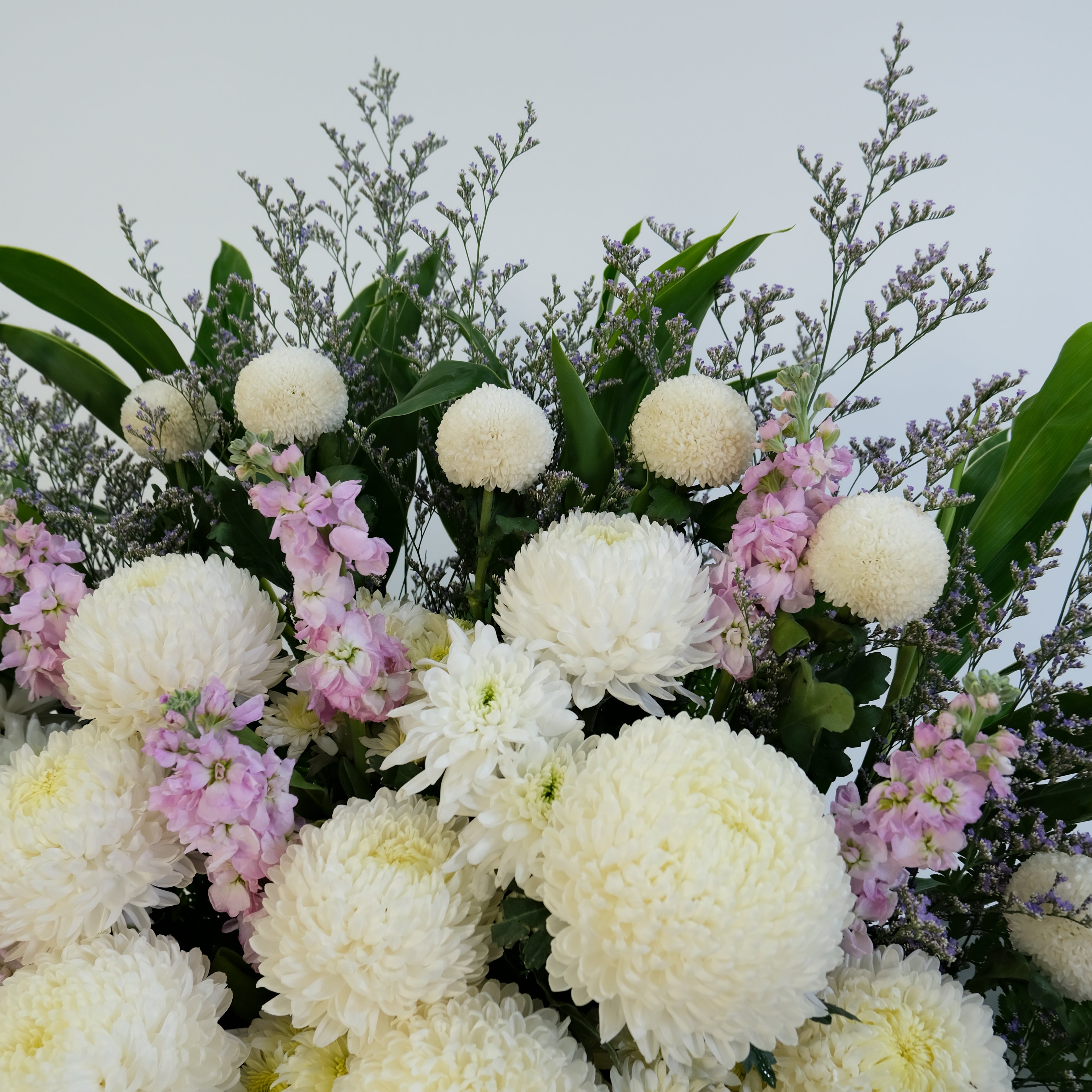 condolence flower stand of white and pink flowers with green leaves on a light gray background