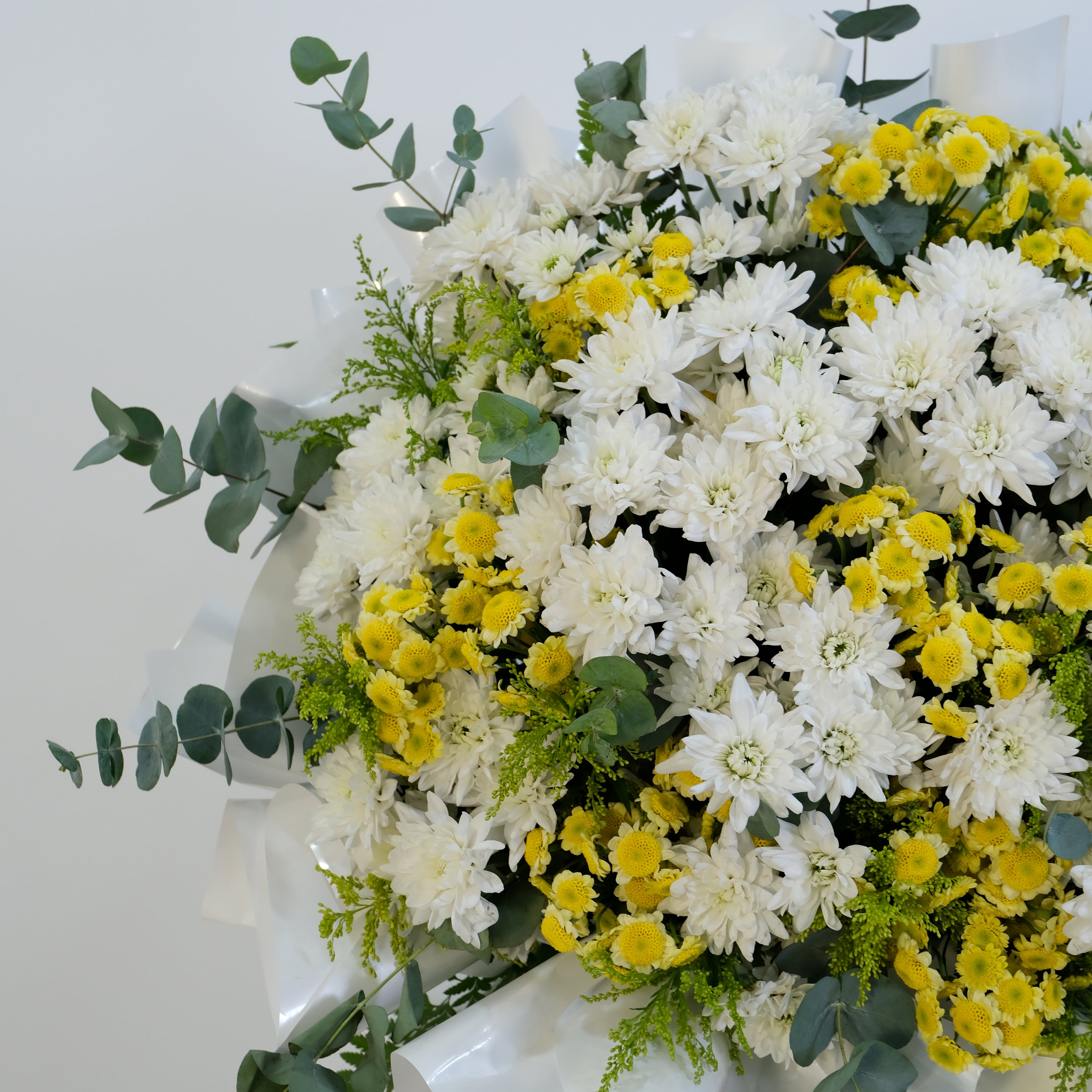 Floral arrangement with white and yellow flowers and greenery on a white background