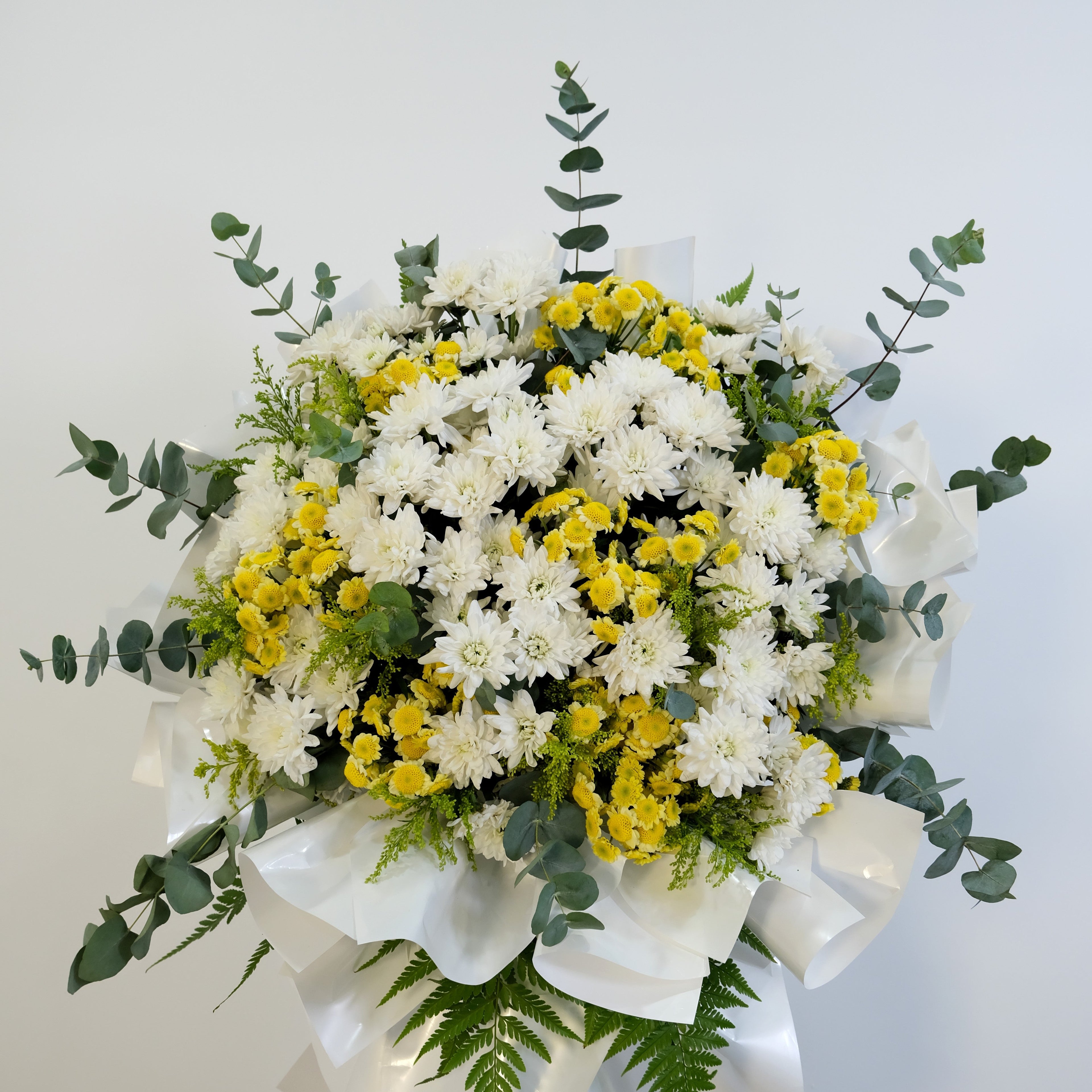 condolence flower stand of white and yellow flowers with greenery on a white background