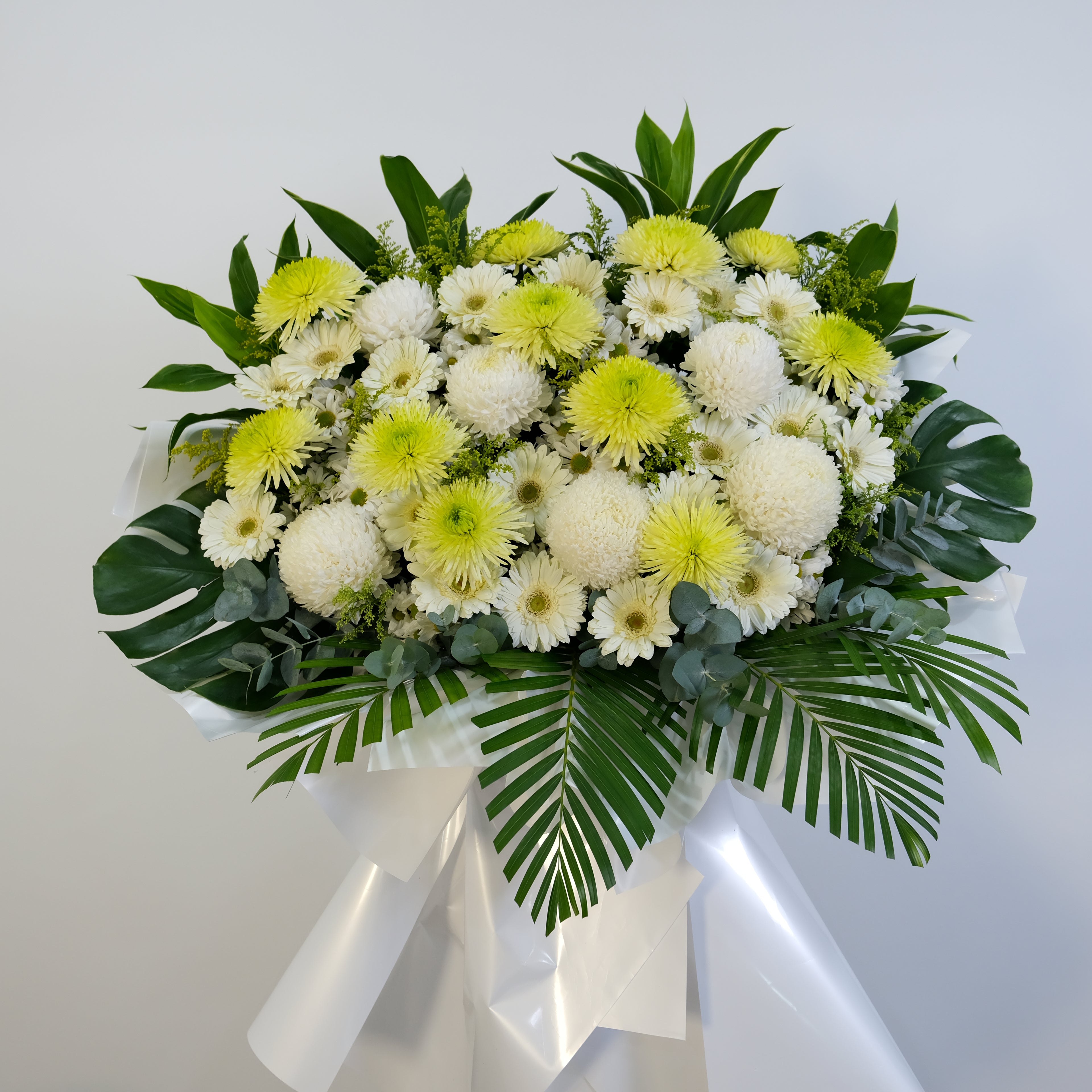 condolence flower stand of white and yellow flowers with green leaves on a light background