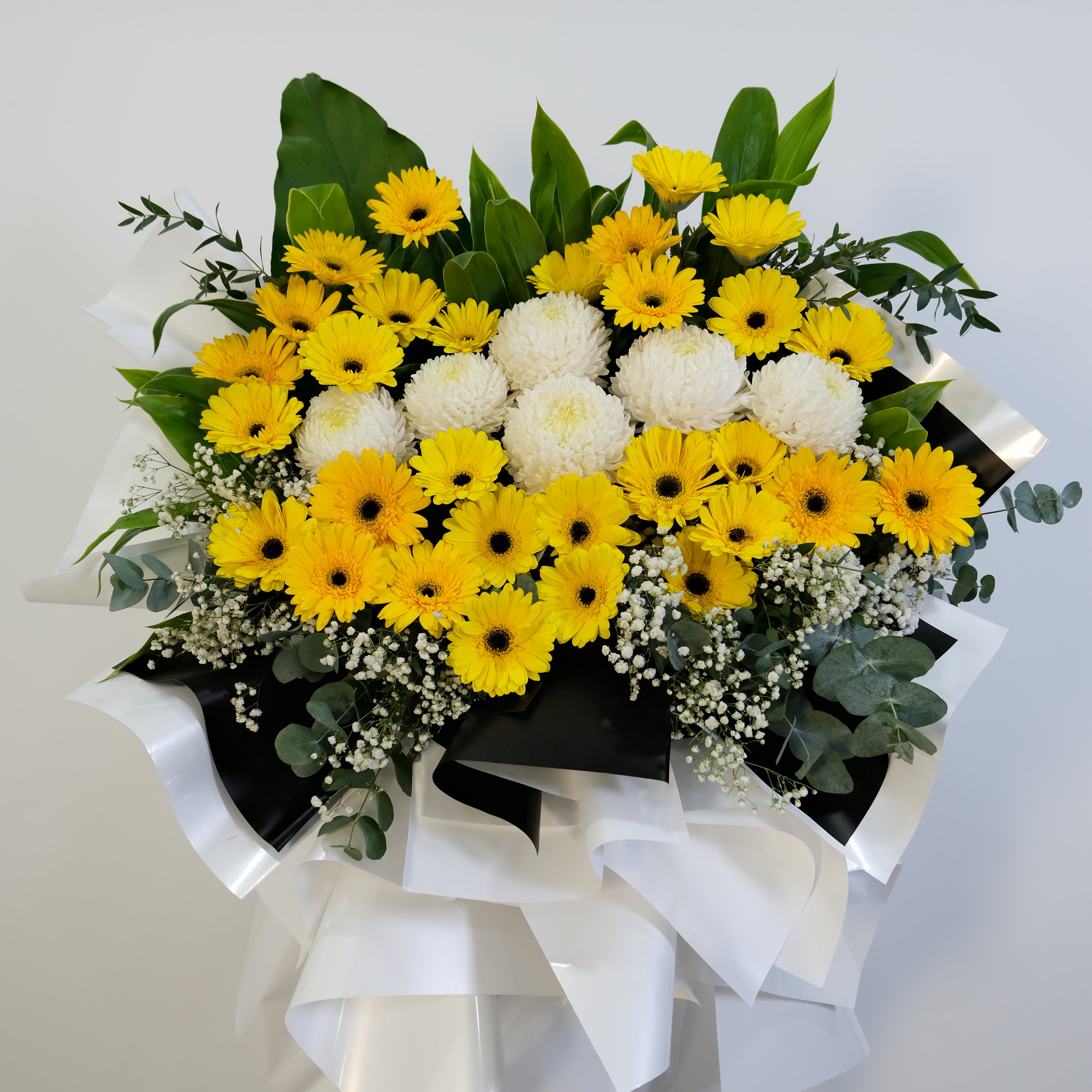 condolence flower stand of yellow and white flowers with greenery on a light gray background