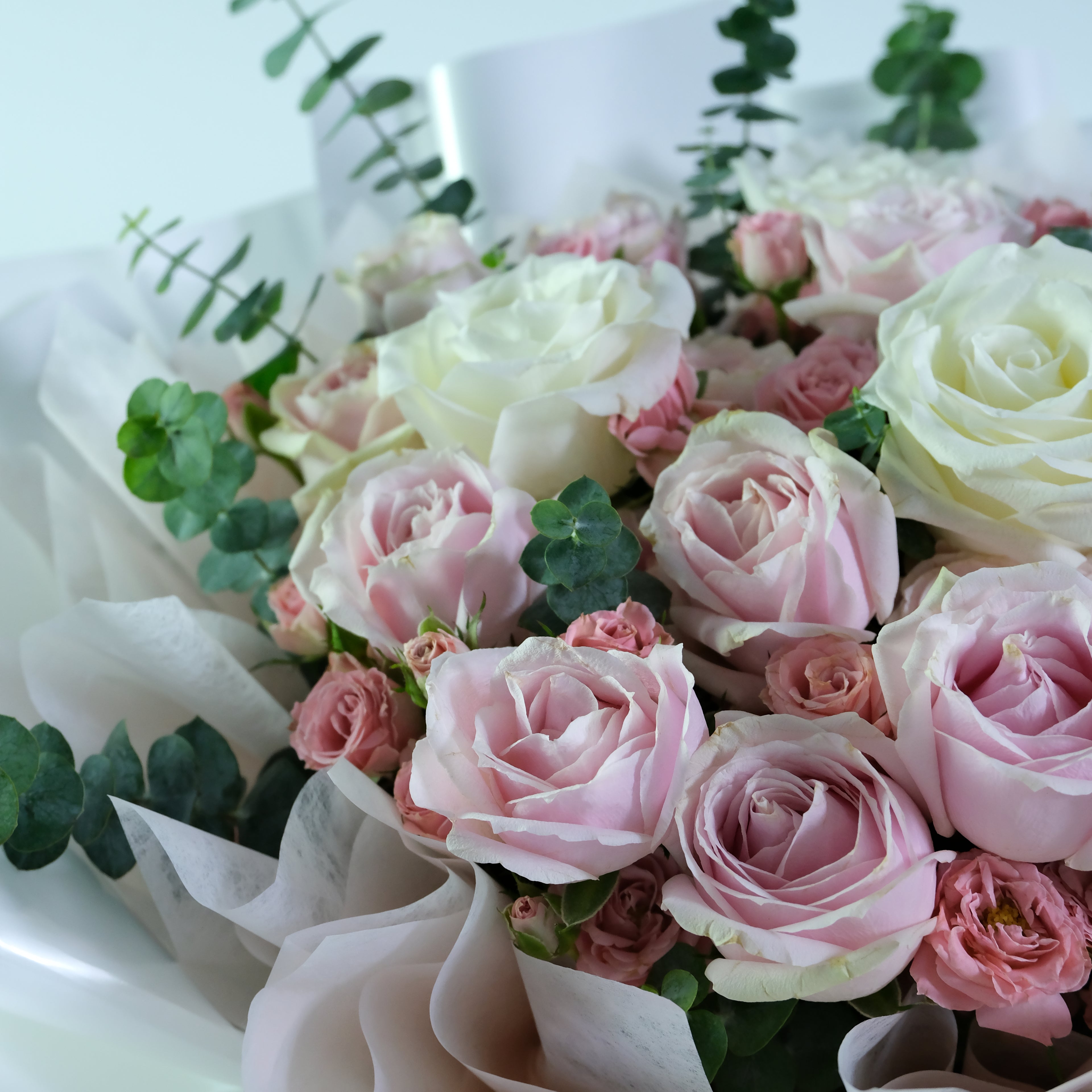 Bouquet of pink and white roses with greenery on a light background