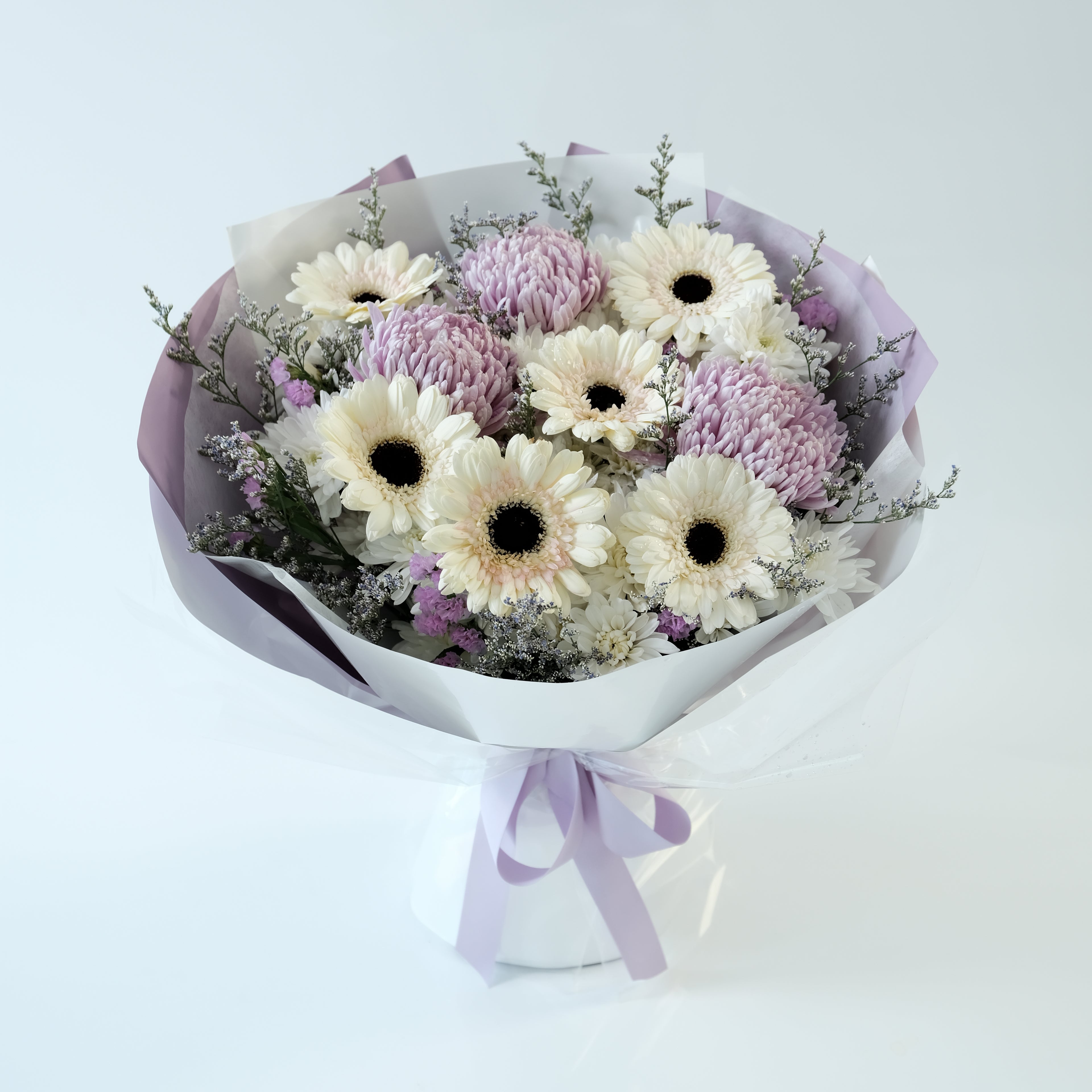 Bouquet of flowers wrapped in purple paper with a white ribbon on a light blue background