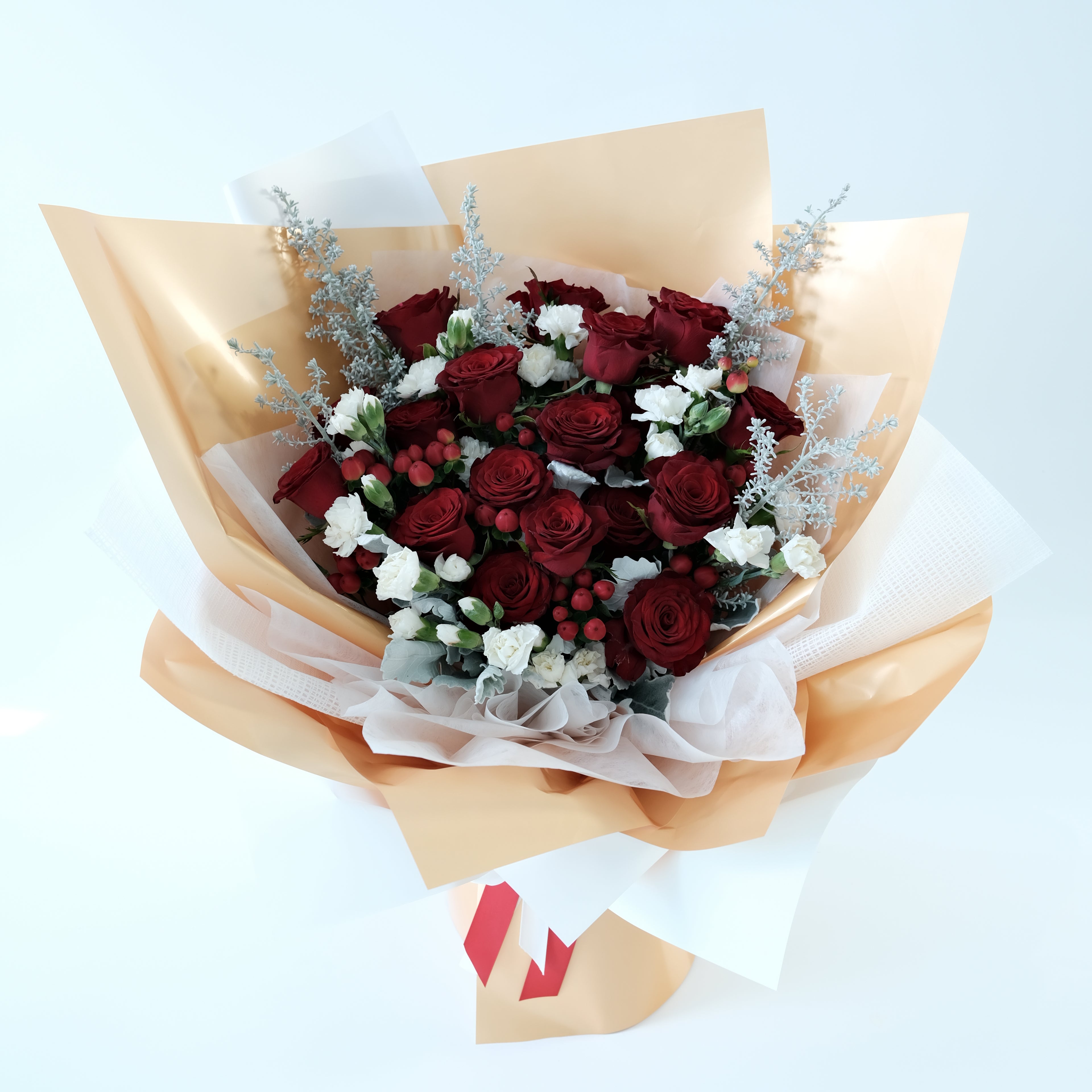 Bouquet of red roses and white flowers wrapped in gold paper on a light blue background