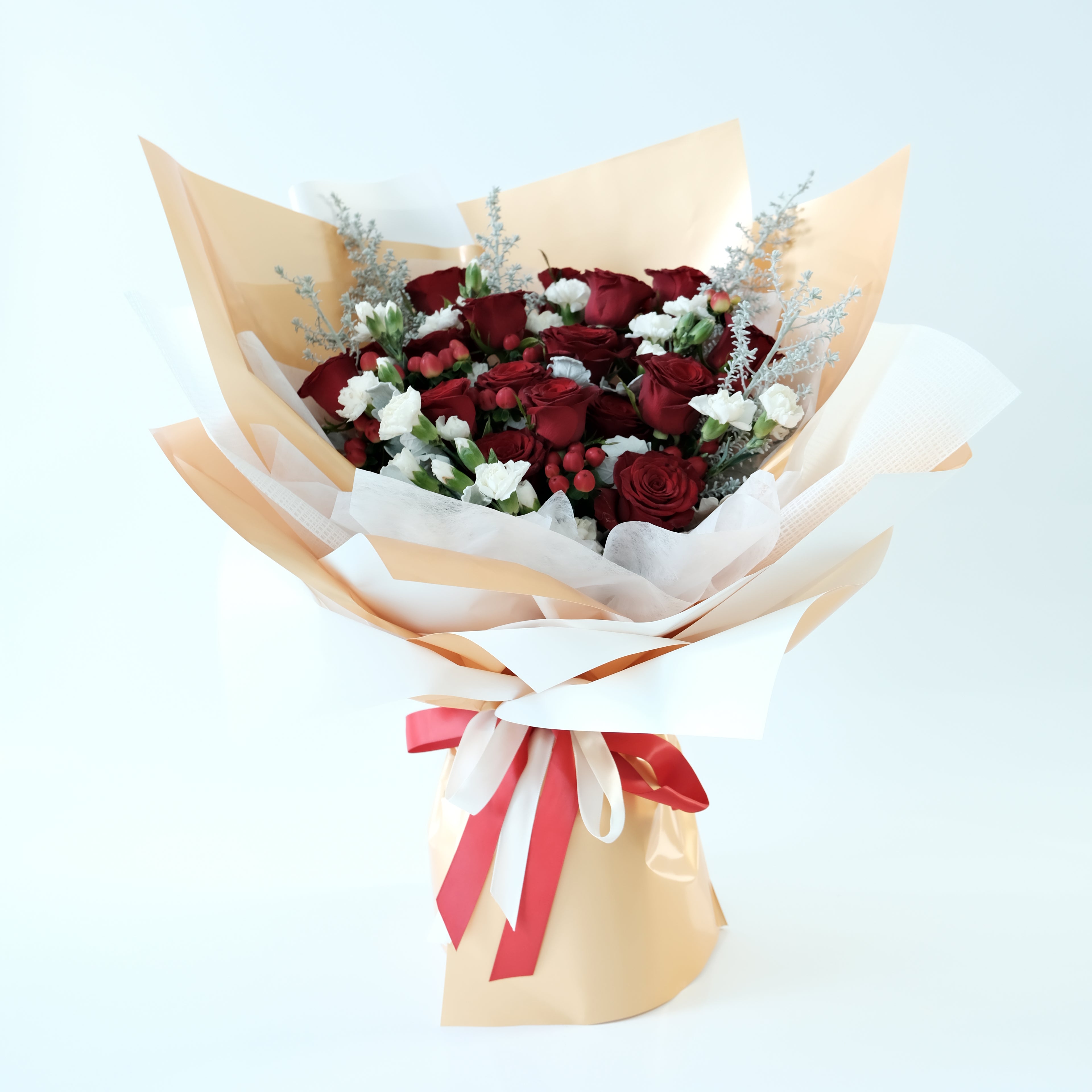 Bouquet of red roses with white accents wrapped in gold paper and a red ribbon on a light gray background