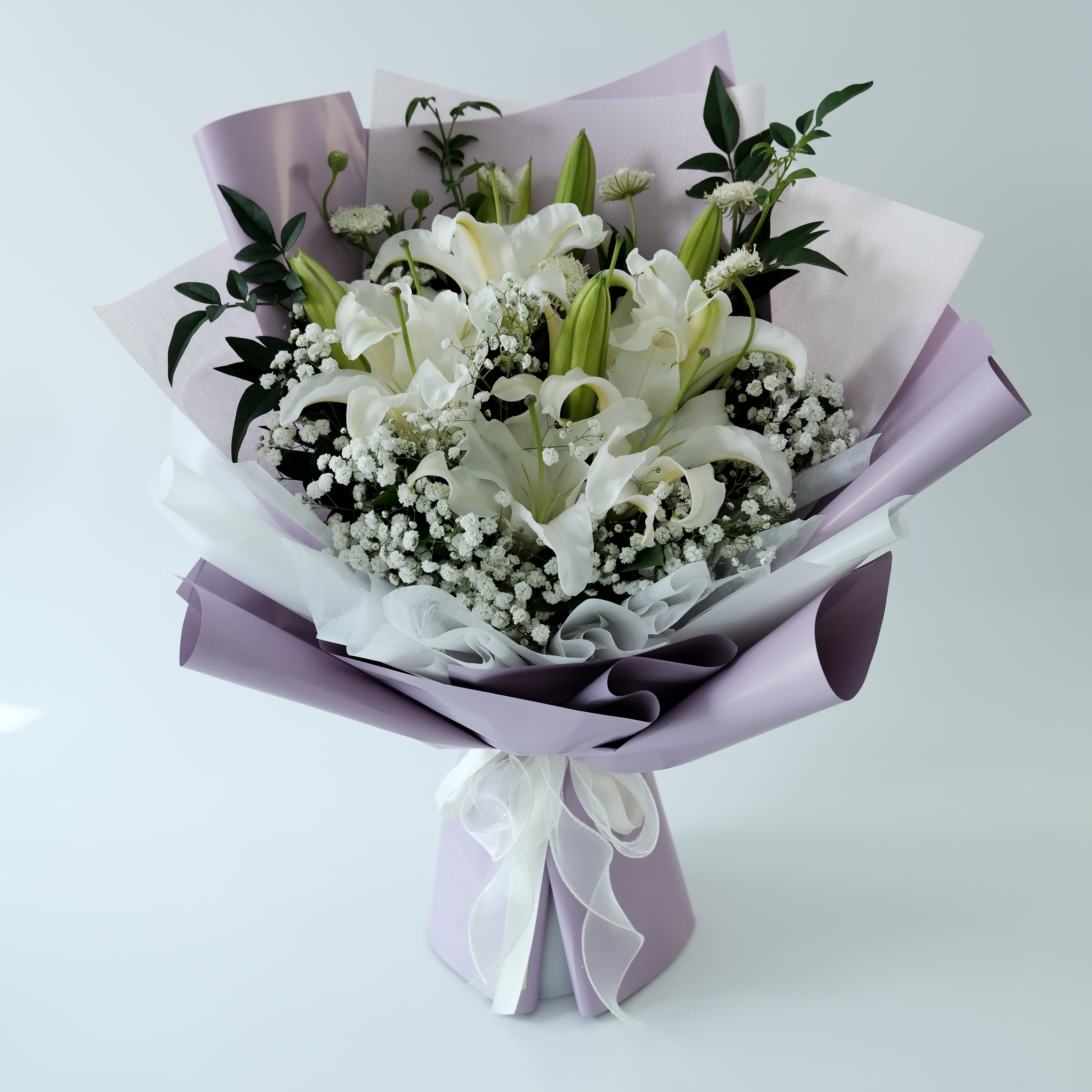 Bouquet of white flowers with green leaves and a purple ribbon on a light gray background