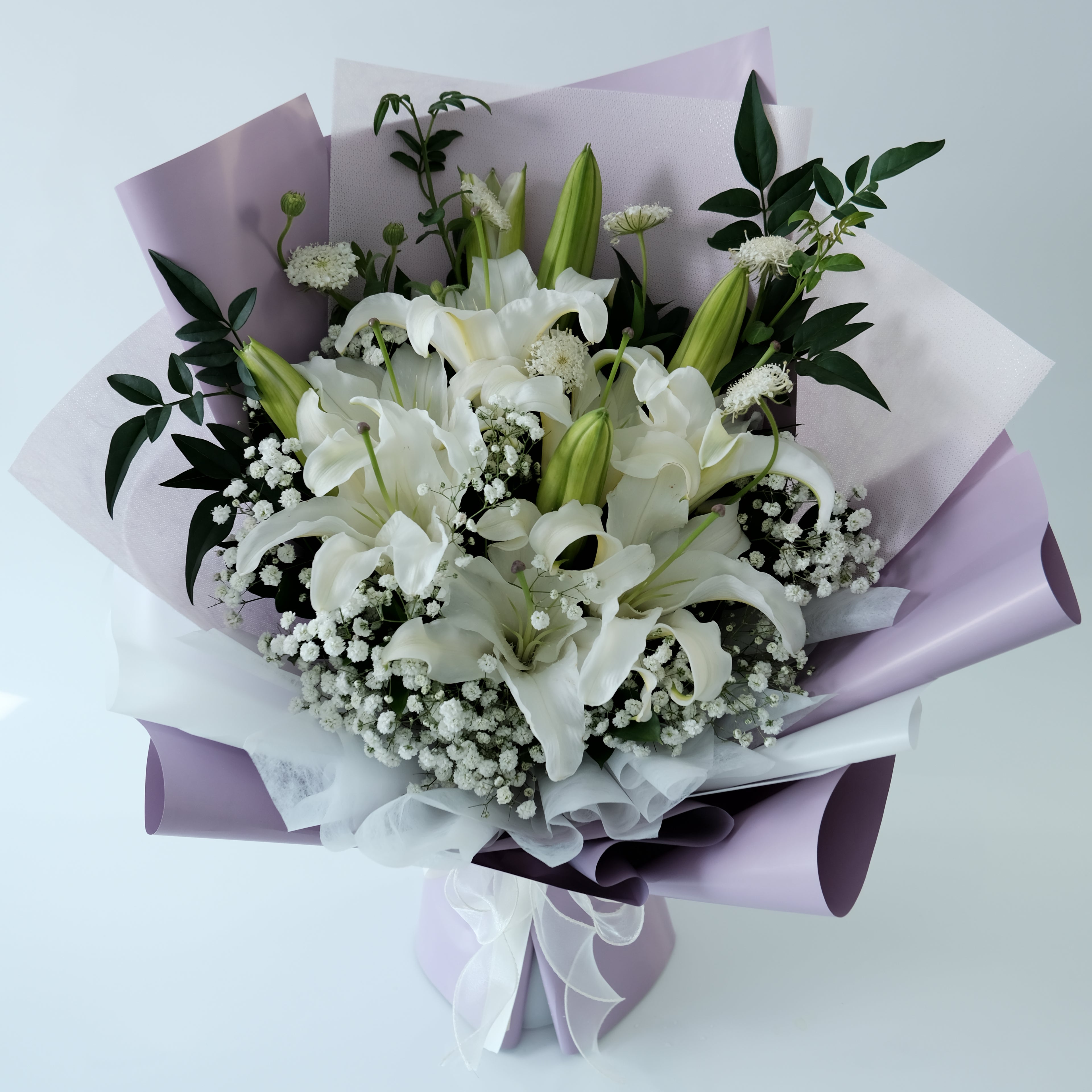 Bouquet of white flowers with green leaves wrapped in purple paper on a light gray background